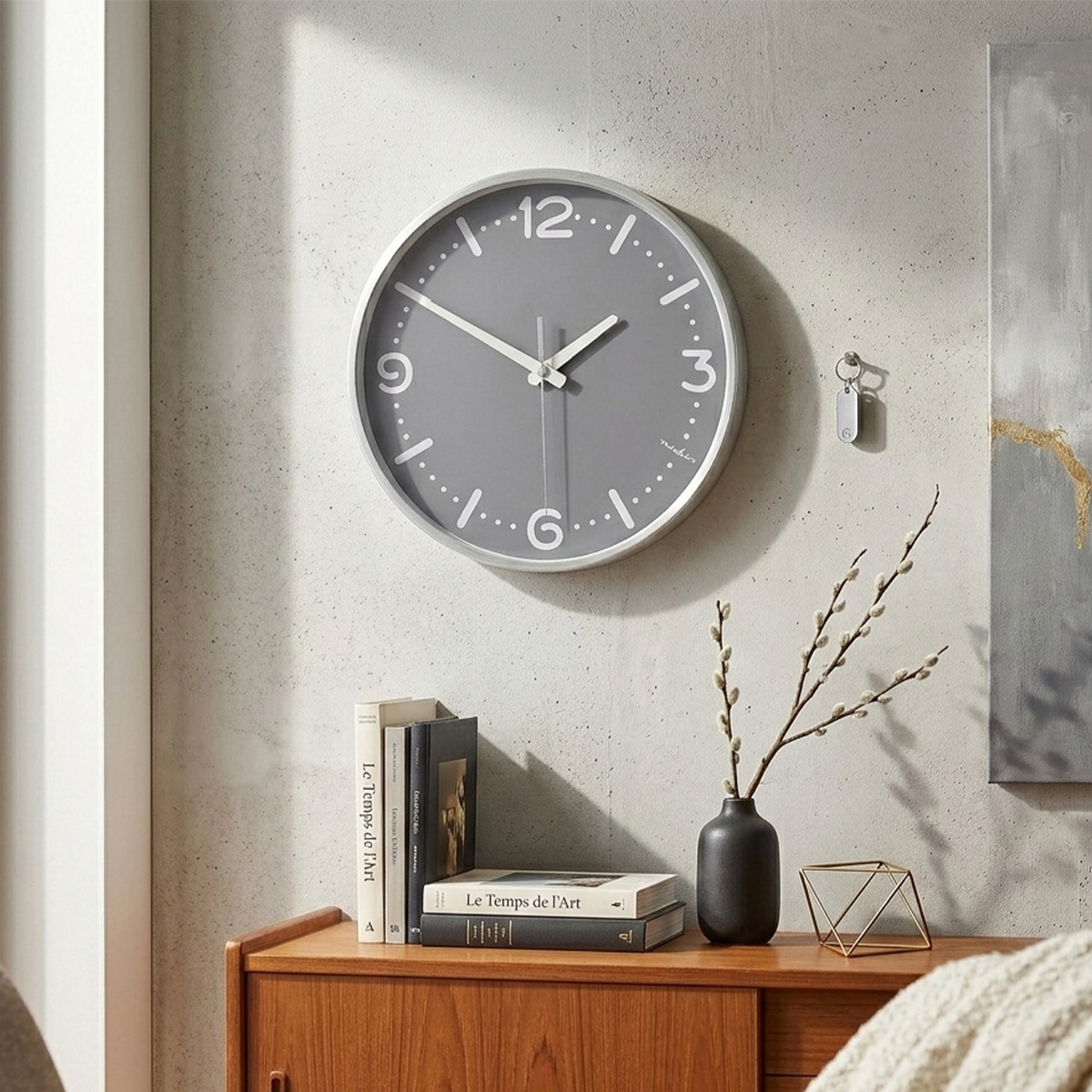 Graue Wanduhr mit weißen Ziffern über einem Holzschrank mit Büchern und Vase.