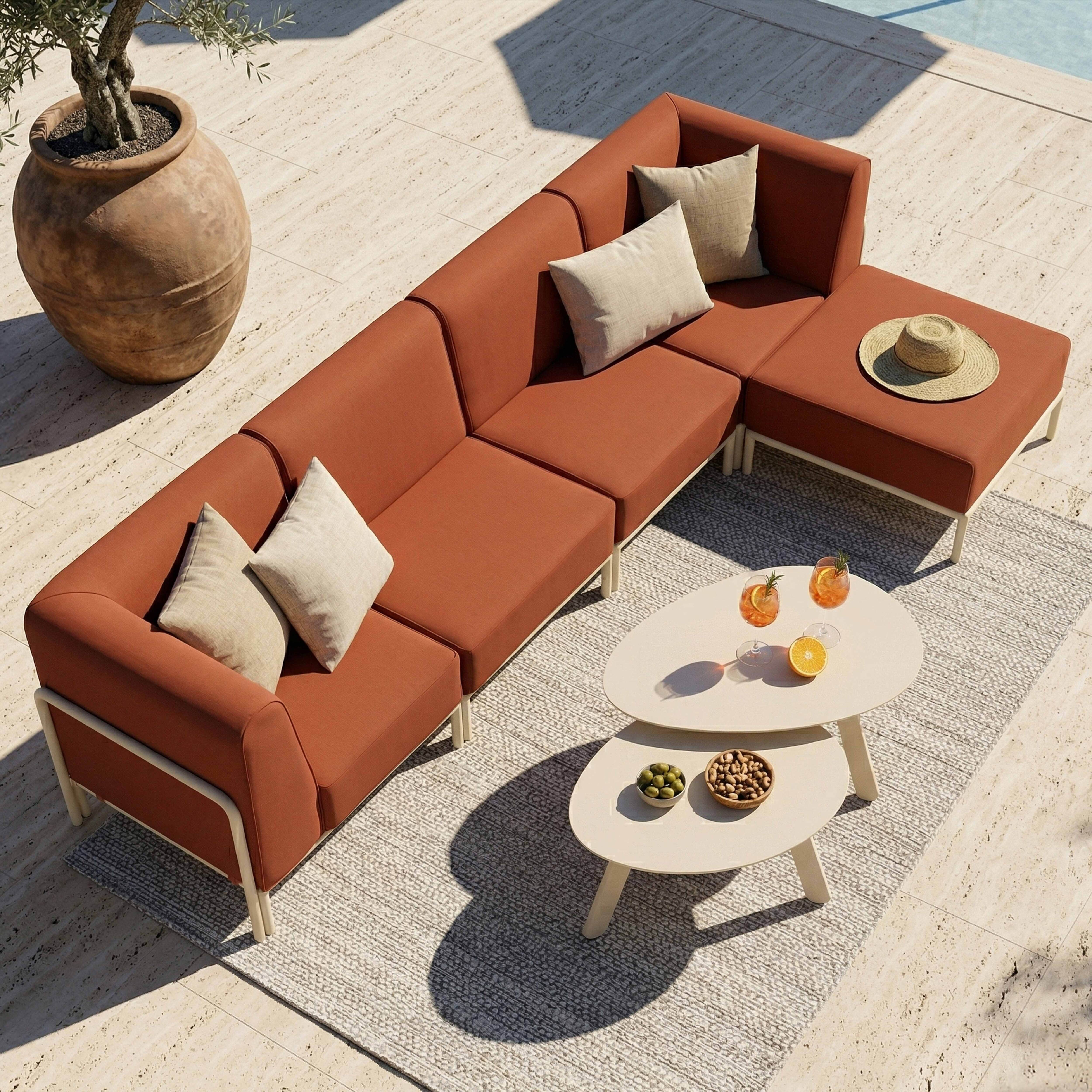 Orange Couch mit Kissen, Beistelltischen und einem Strohhut auf einer Terrasse.