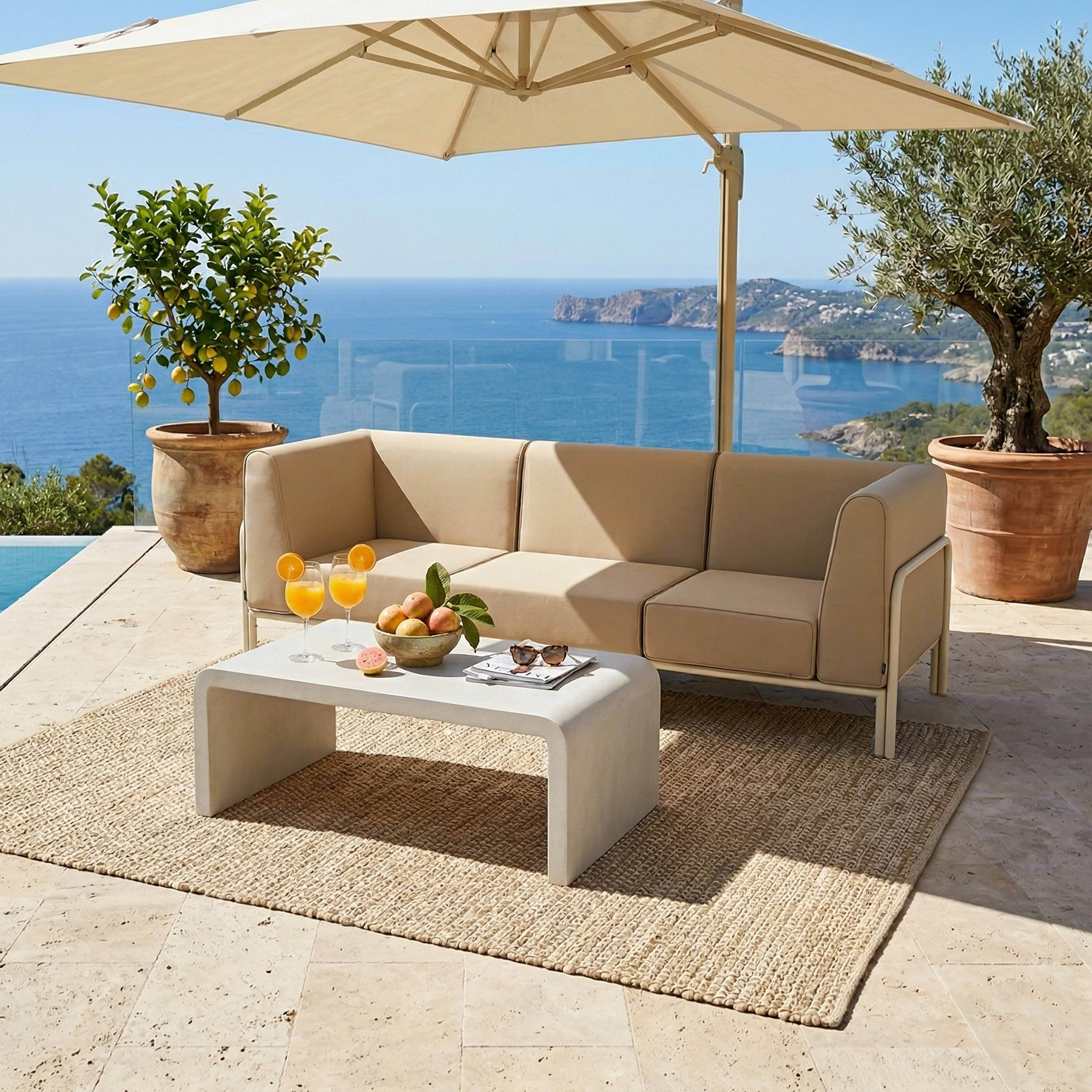 Eine beigefarbene Couch und ein Couchtisch auf einem Teppich mit malerischem Meerblick.