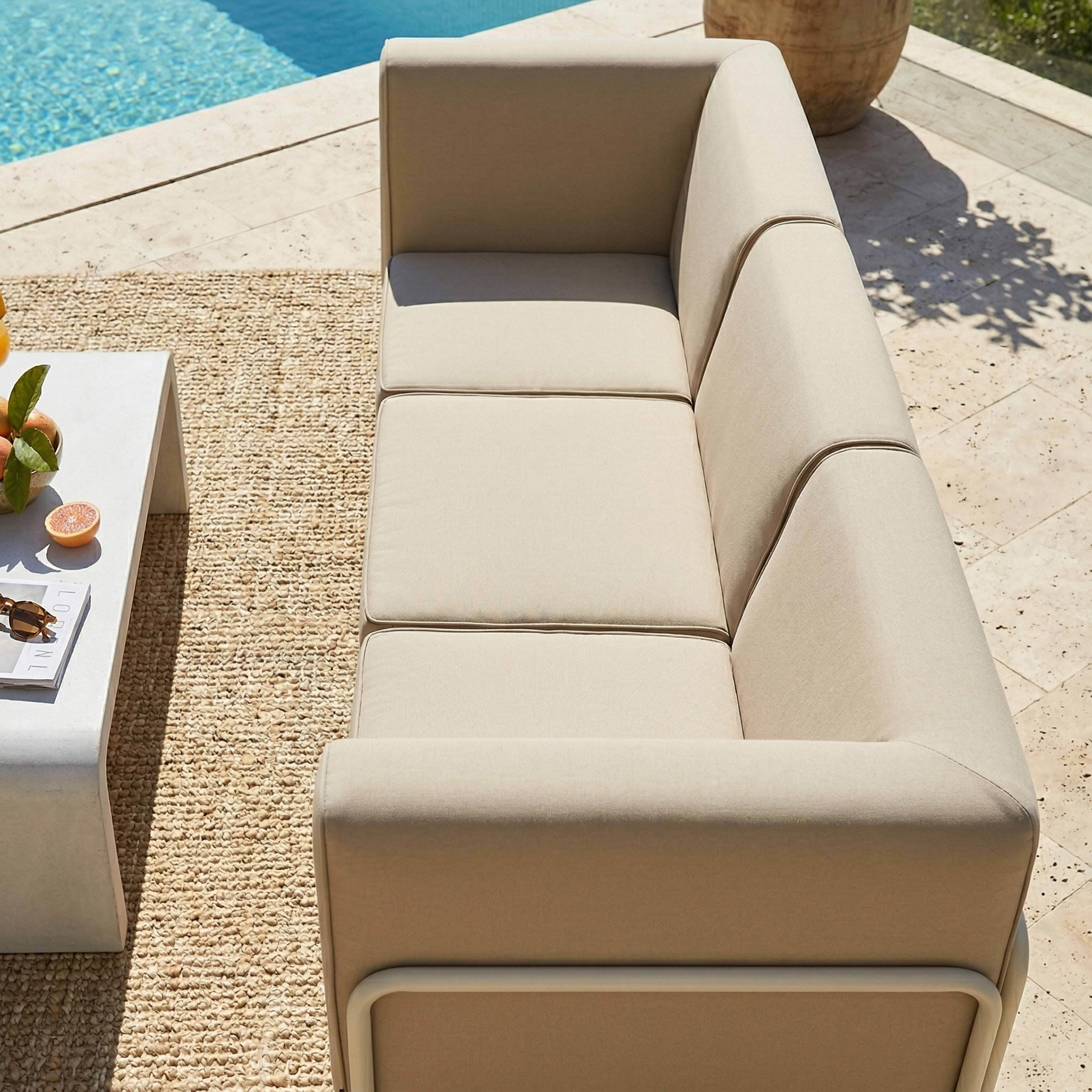 Ein hellbeiger Ecksofa mit weißen Akzenten steht auf einem Teppich neben einem Pool.