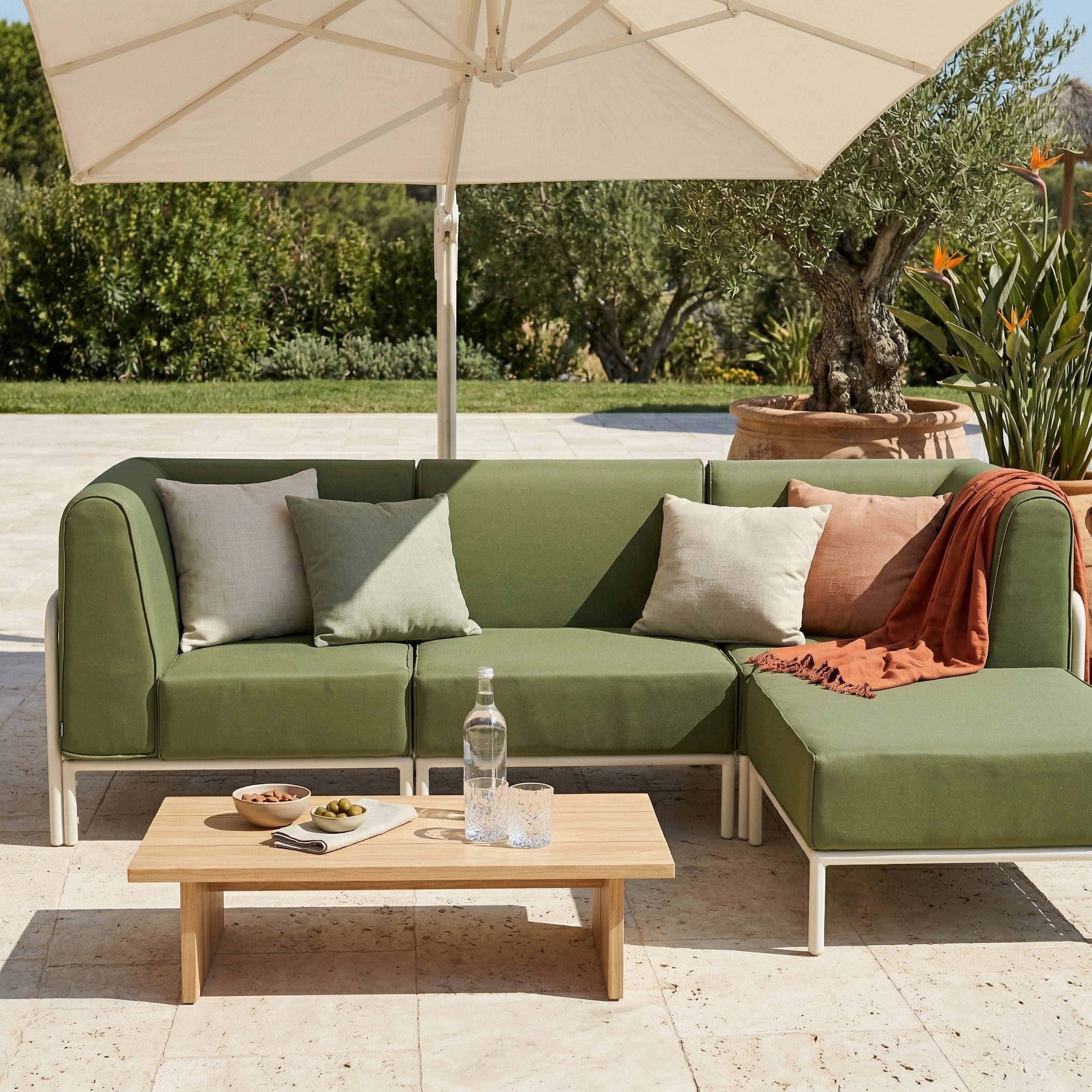 Grünes Ecksofa unter Sonnenschirm mit Holztisch, Getränken und Snacks.