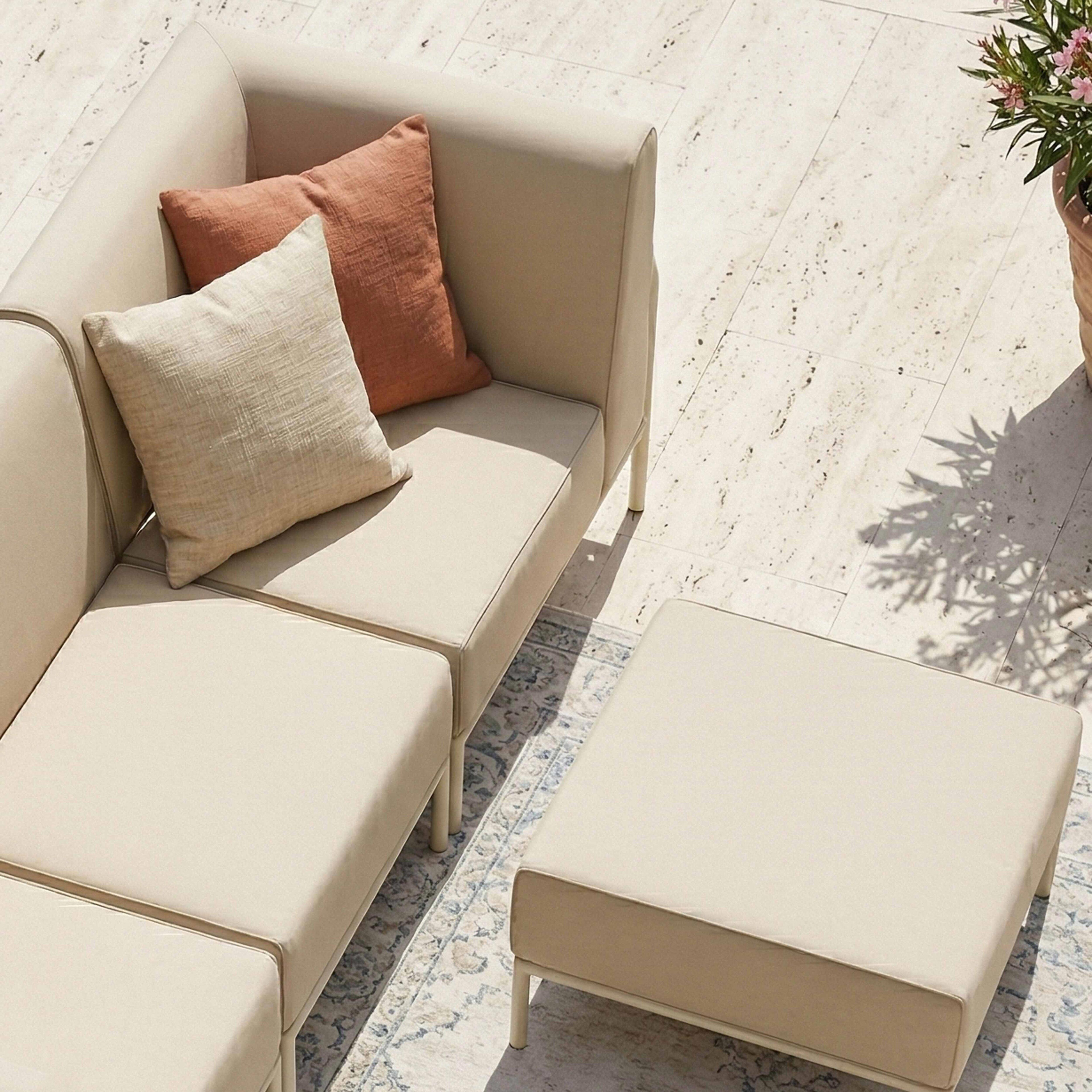 Ein beigefarbenes Ecksofa mit Kissen und einem Hocker auf einer Fliesenoberfläche.