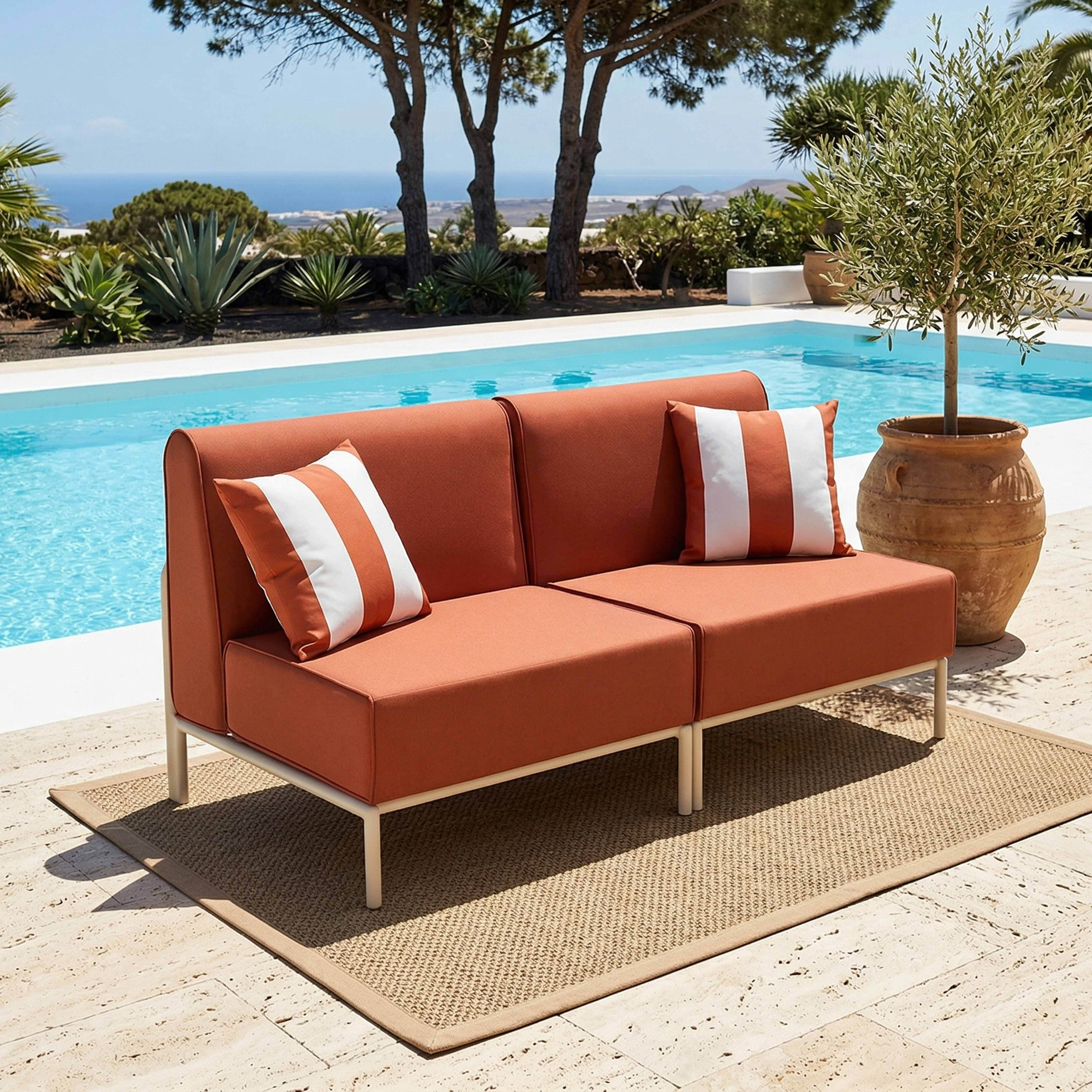 Orange Couch mit Streifen-Kissen neben Pool, mediterrane Pflanzen.
