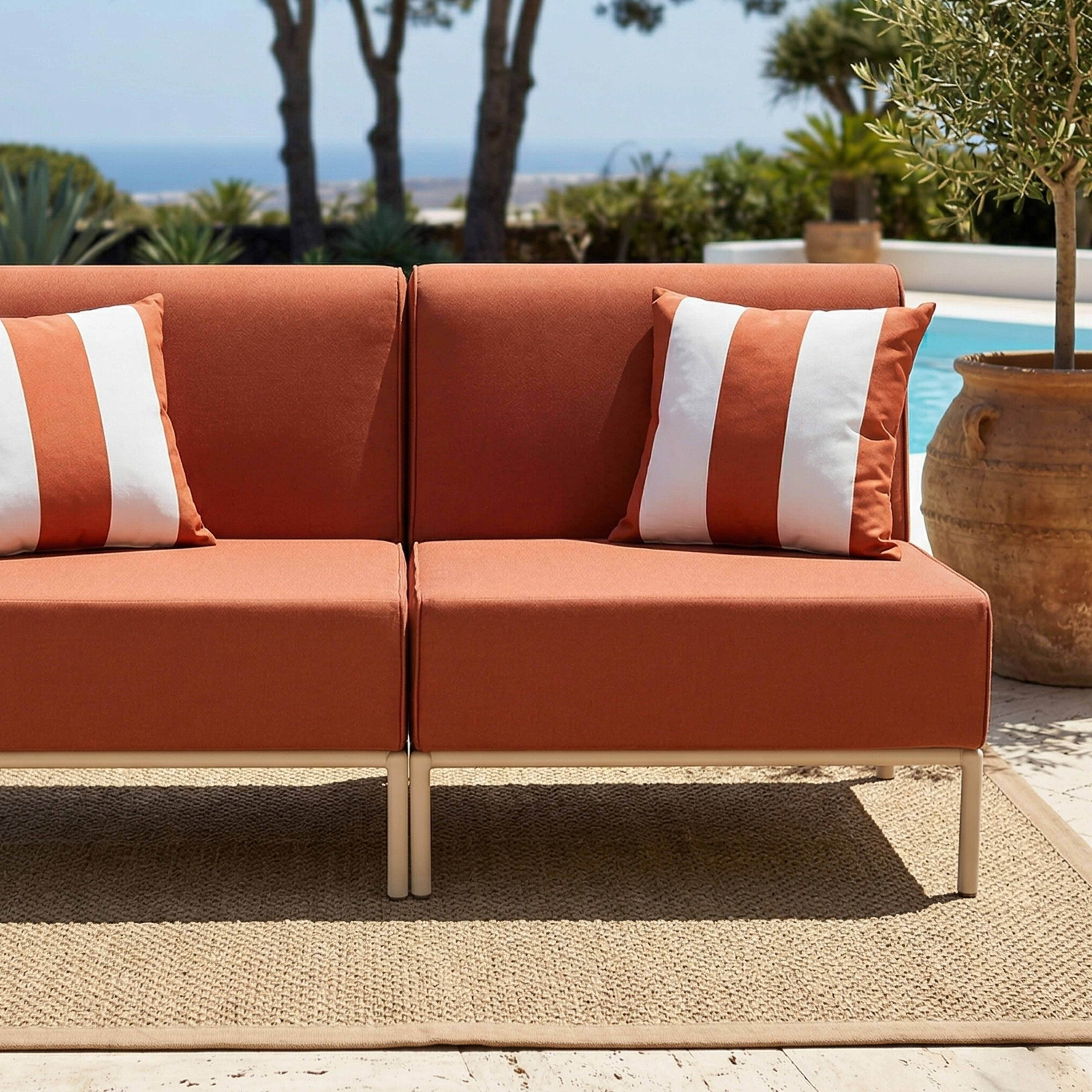 Ein orangefarbenes Sofa mit weißen Streifenpolstern am Pool mit Meerblick.