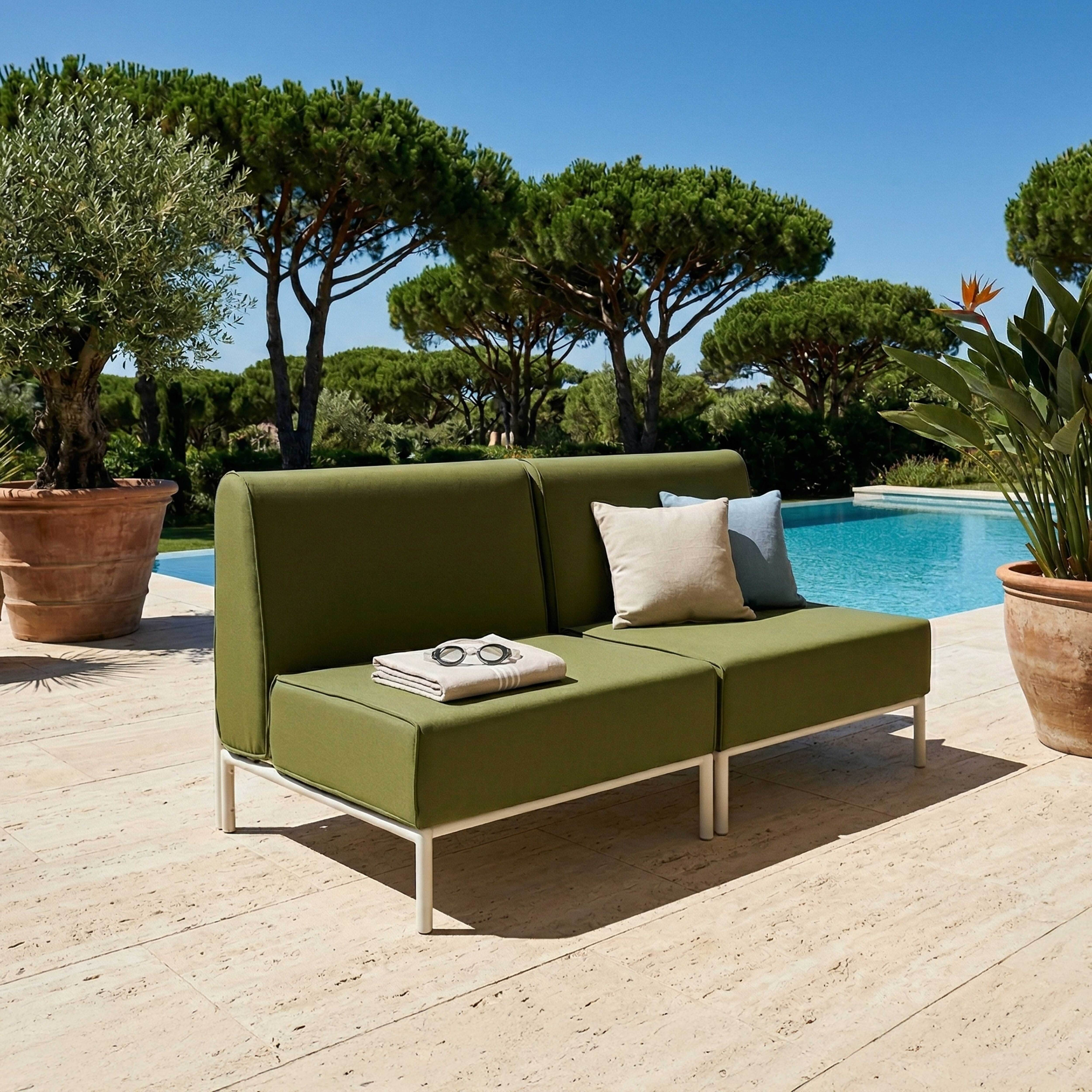 Grünes Outdoor-Sofa am Pool mit Kissen und Decke. Bäume im Hintergrund.