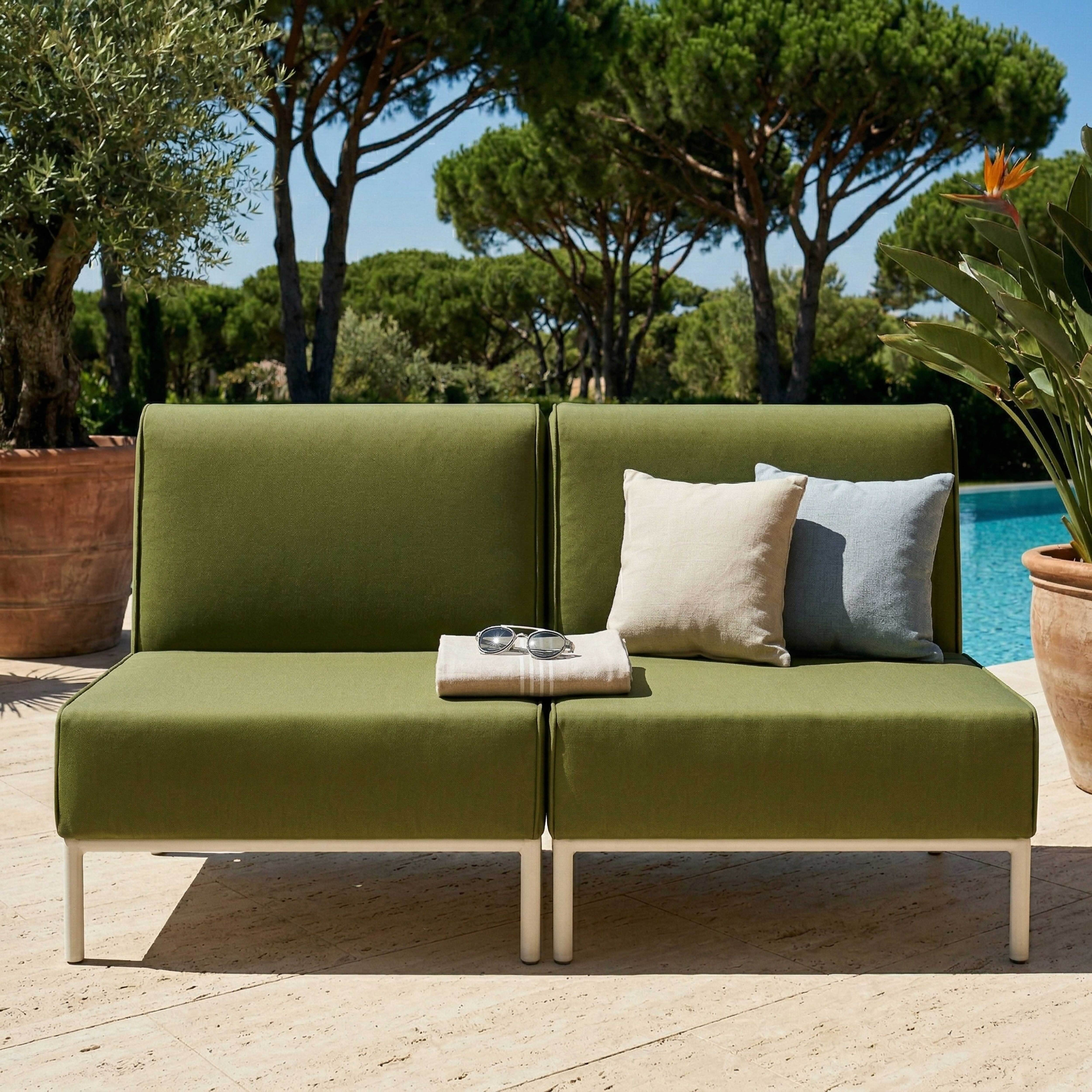 Ein grünes Outdoor-Sofa mit Kissen und einer Decke am Pool.