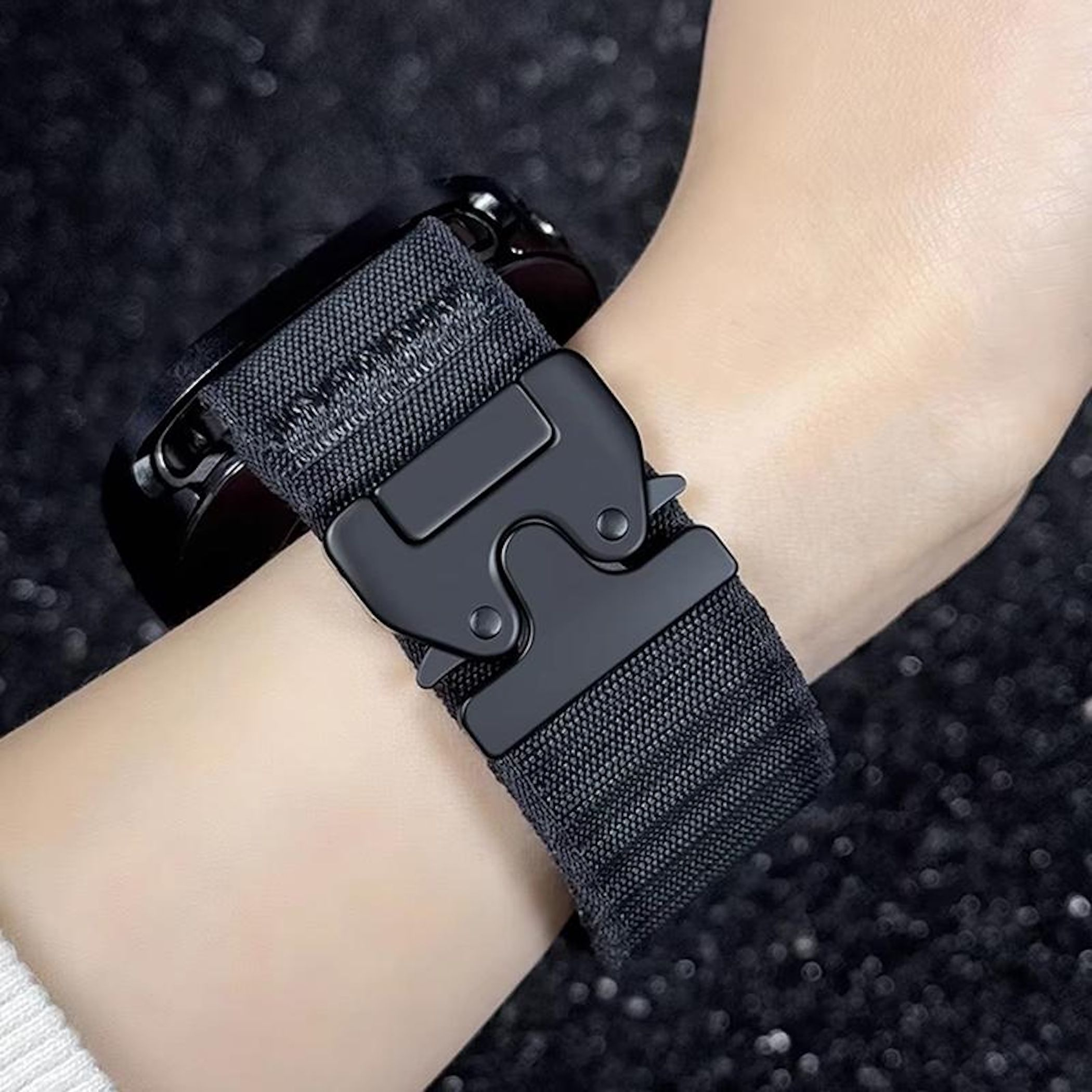 Ein schwarzes Stoffarmband mit Metallschnalle an einem Handgelenk, dunkler Hintergrund.