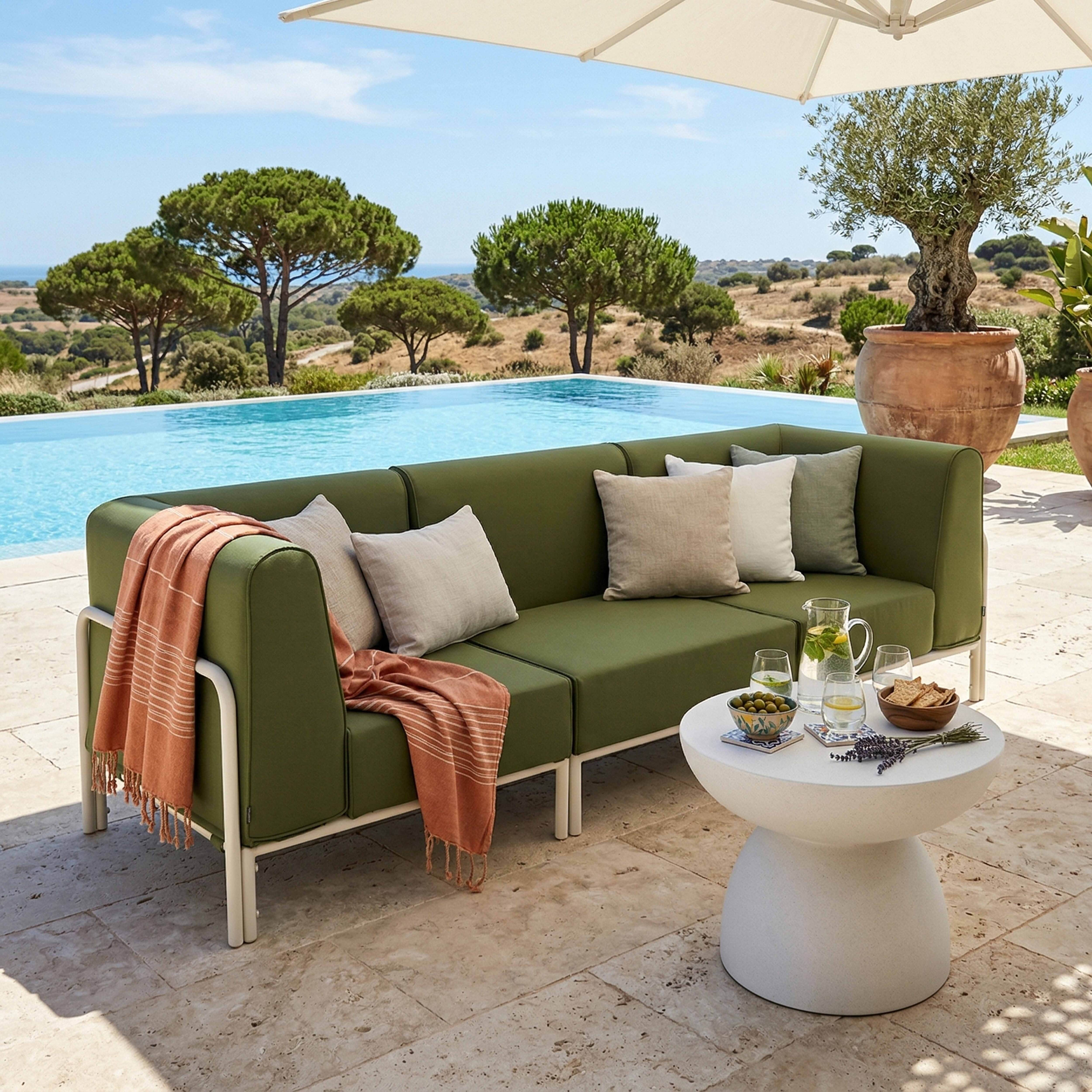 Grüne Outdoormöbel-Couch am Pool mit Getränken, Snacks und einem Terrakotta-Olivenbaum.