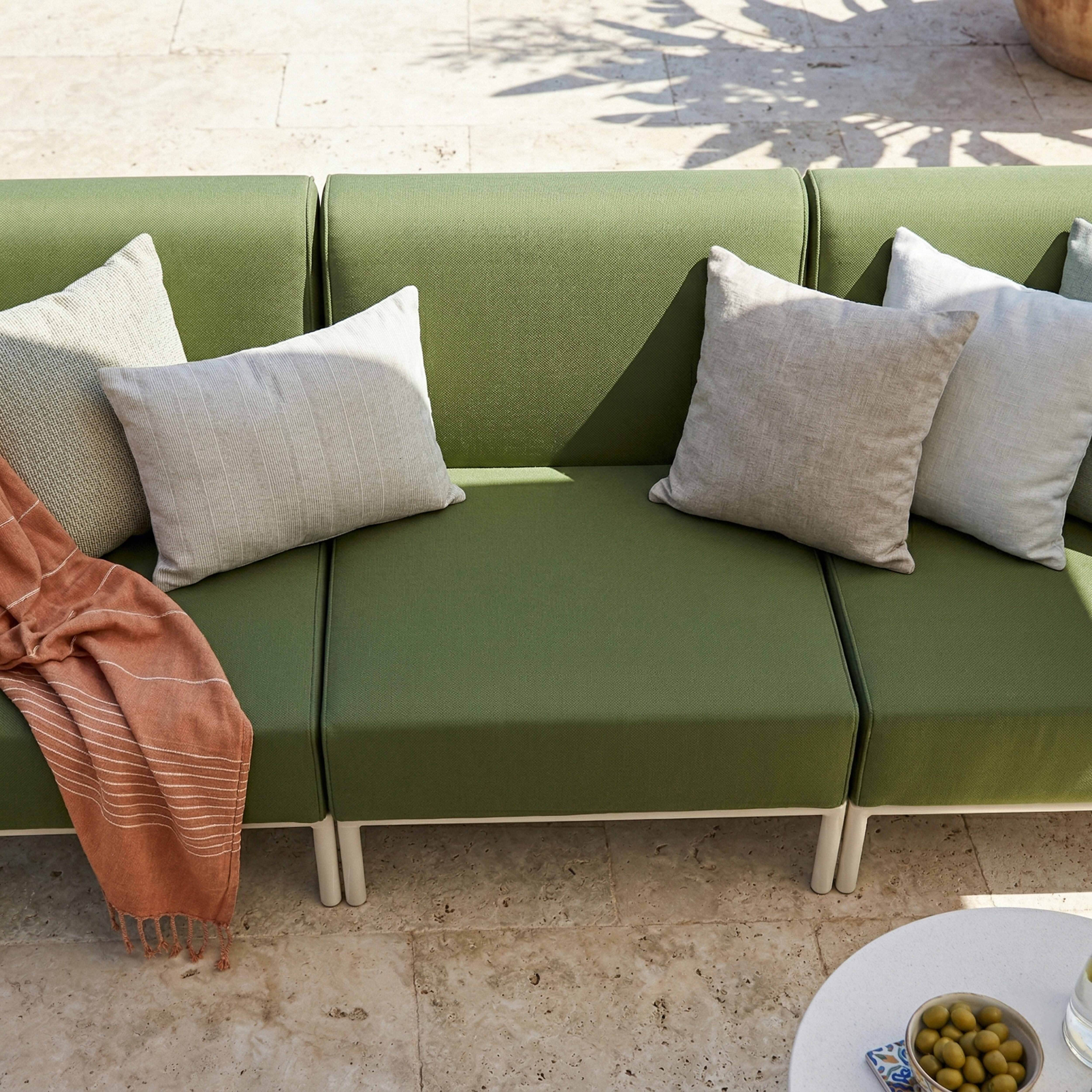 Ein grünes Sofa mit Kissen und einer Decke auf einer Steinveranda.