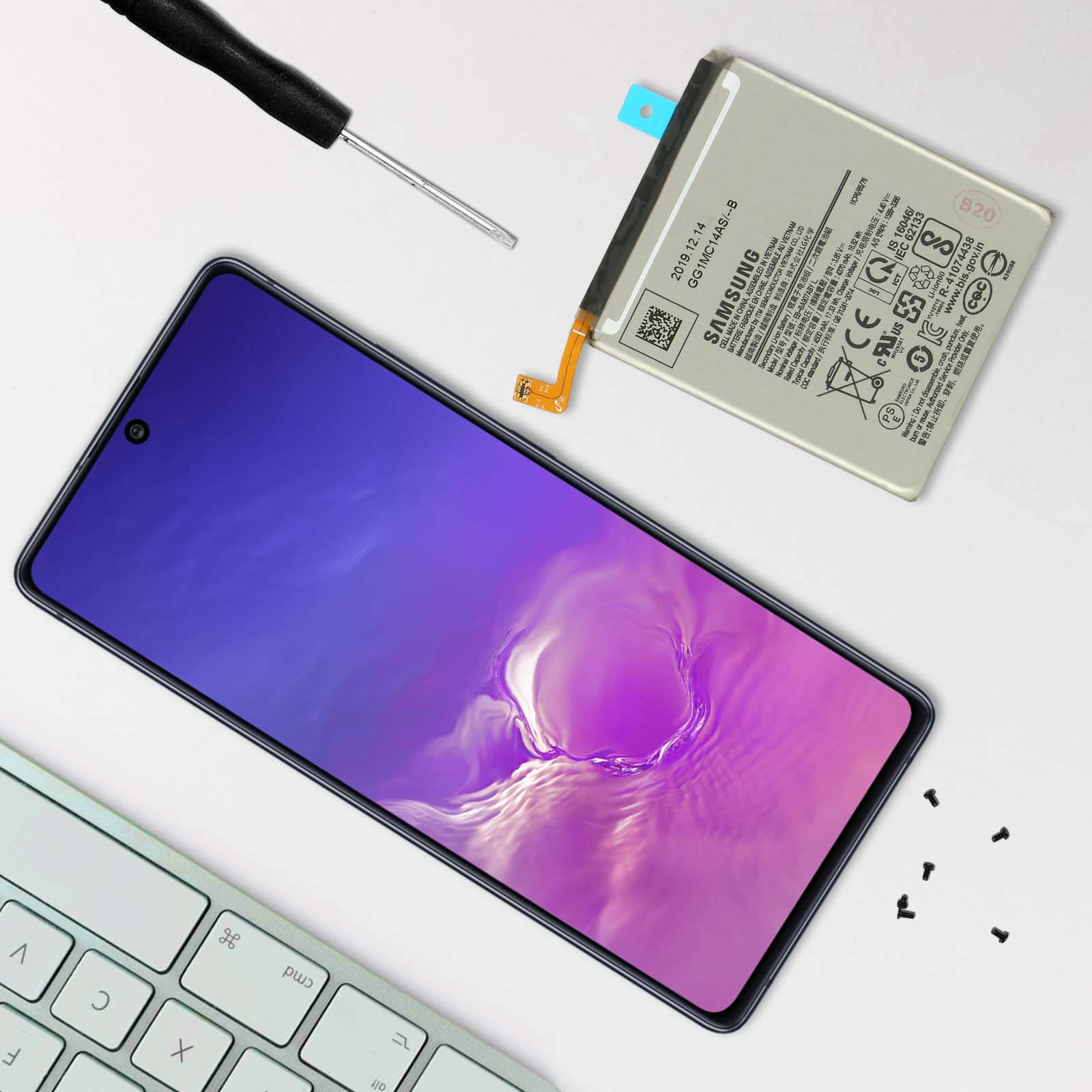 Uno smartphone, batteria, cacciavite e tastiera su sfondo bianco.