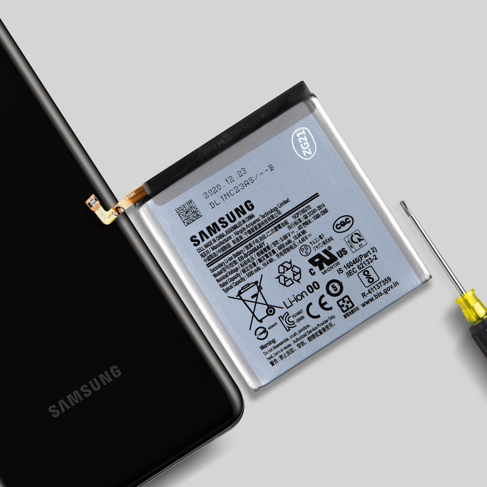 Una batteria Samsung giace accanto a uno smartphone e un cacciavite.