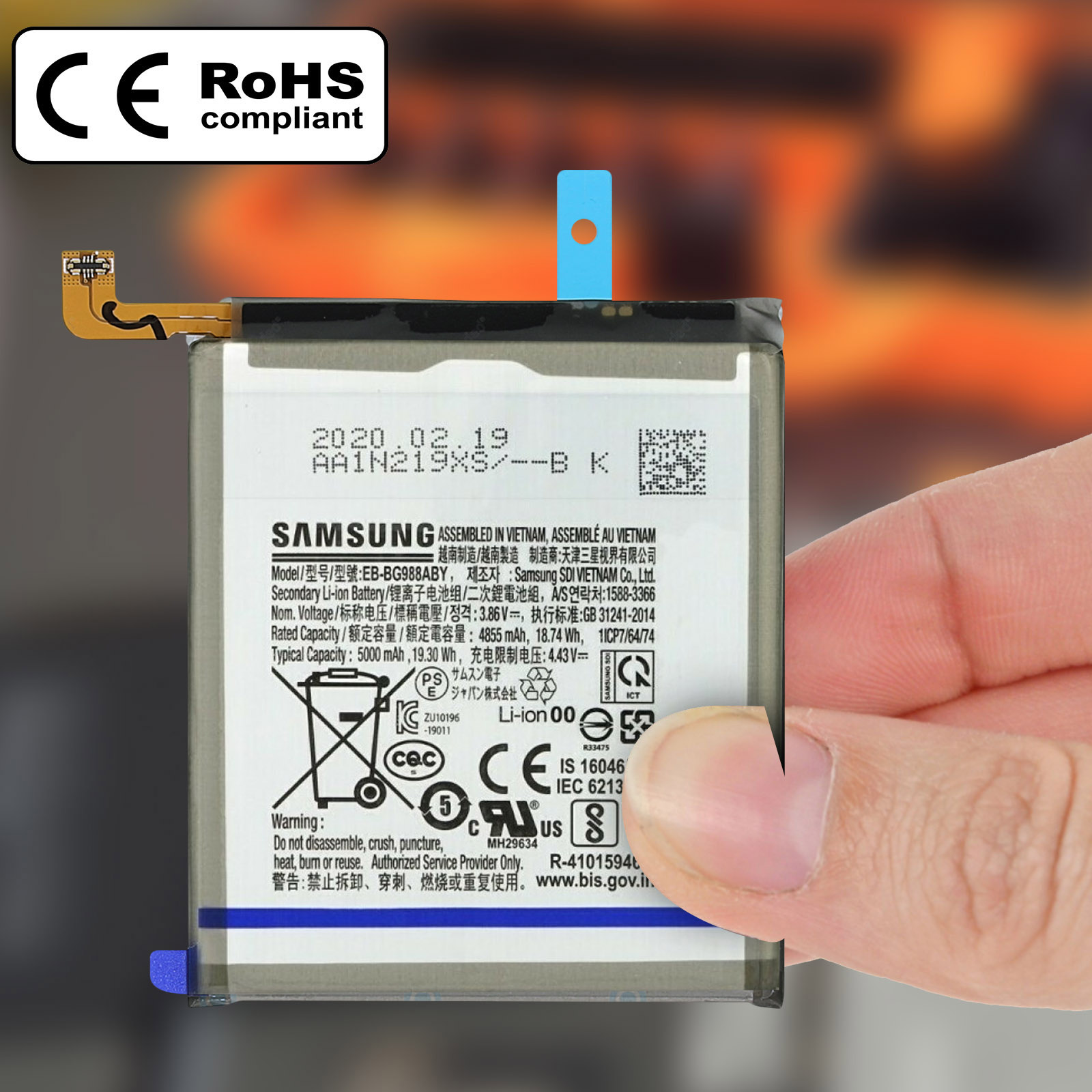 Une main tient une batterie Li-Ion Samsung EB-BG988ABY avec les marques de conformité CE et RoHS.