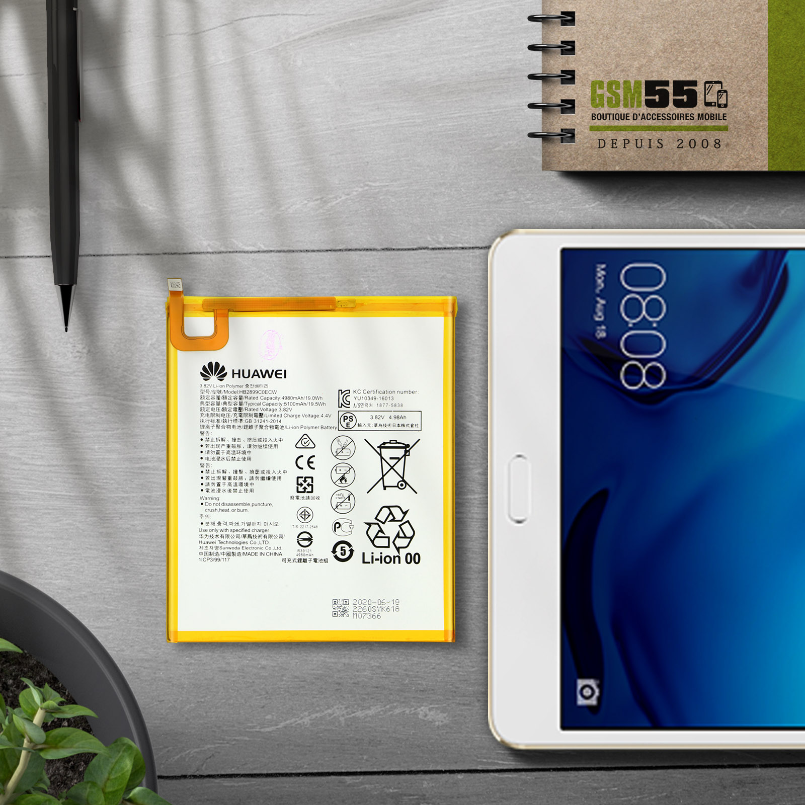 Batteria e tablet Huawei su superficie grigia, accanto a un taccuino.