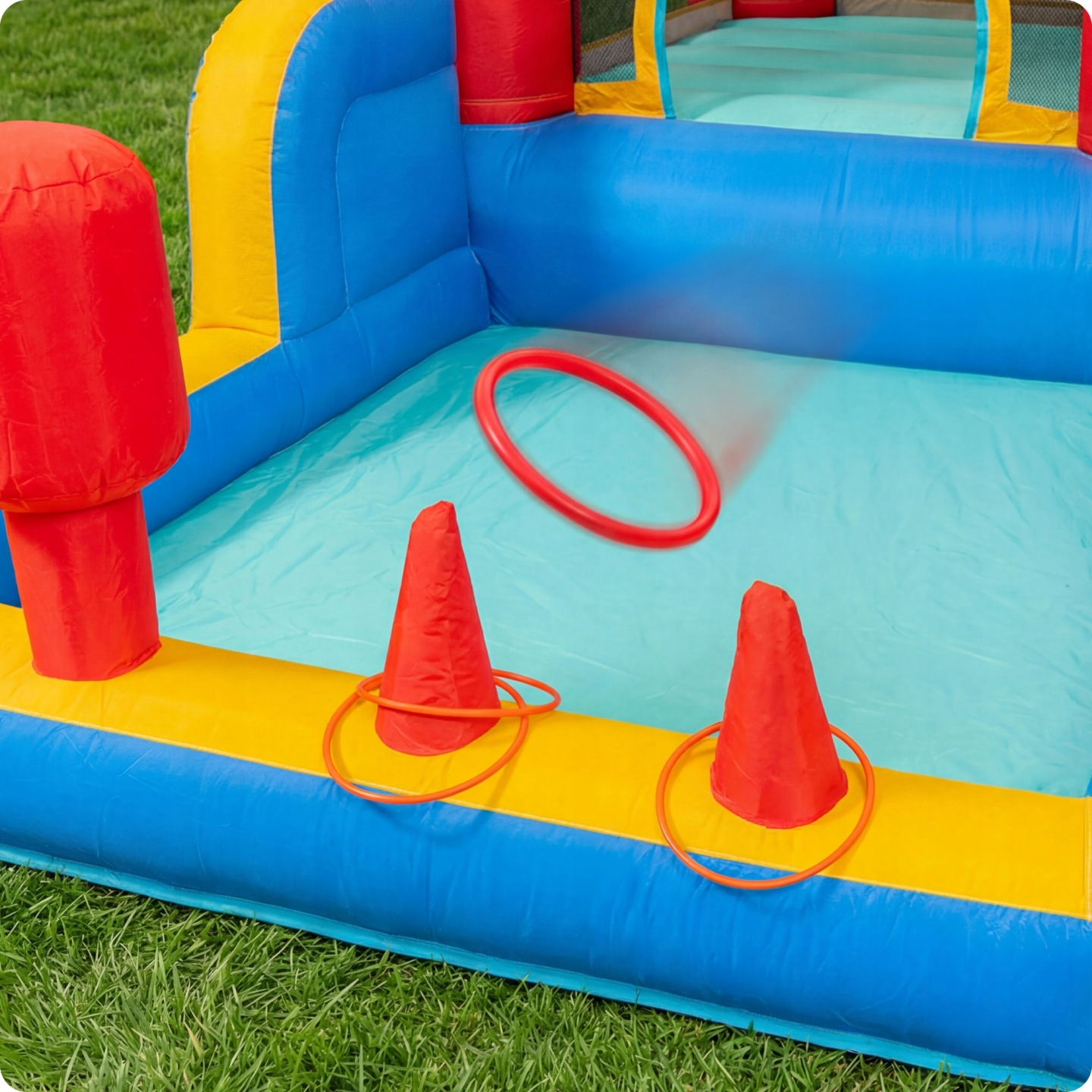 Ein aufblasbarer Spielbereich mit roten, gelben und blauen Abschnitten. Zwei rote Kegel mit Ringen sind aufgestellt.