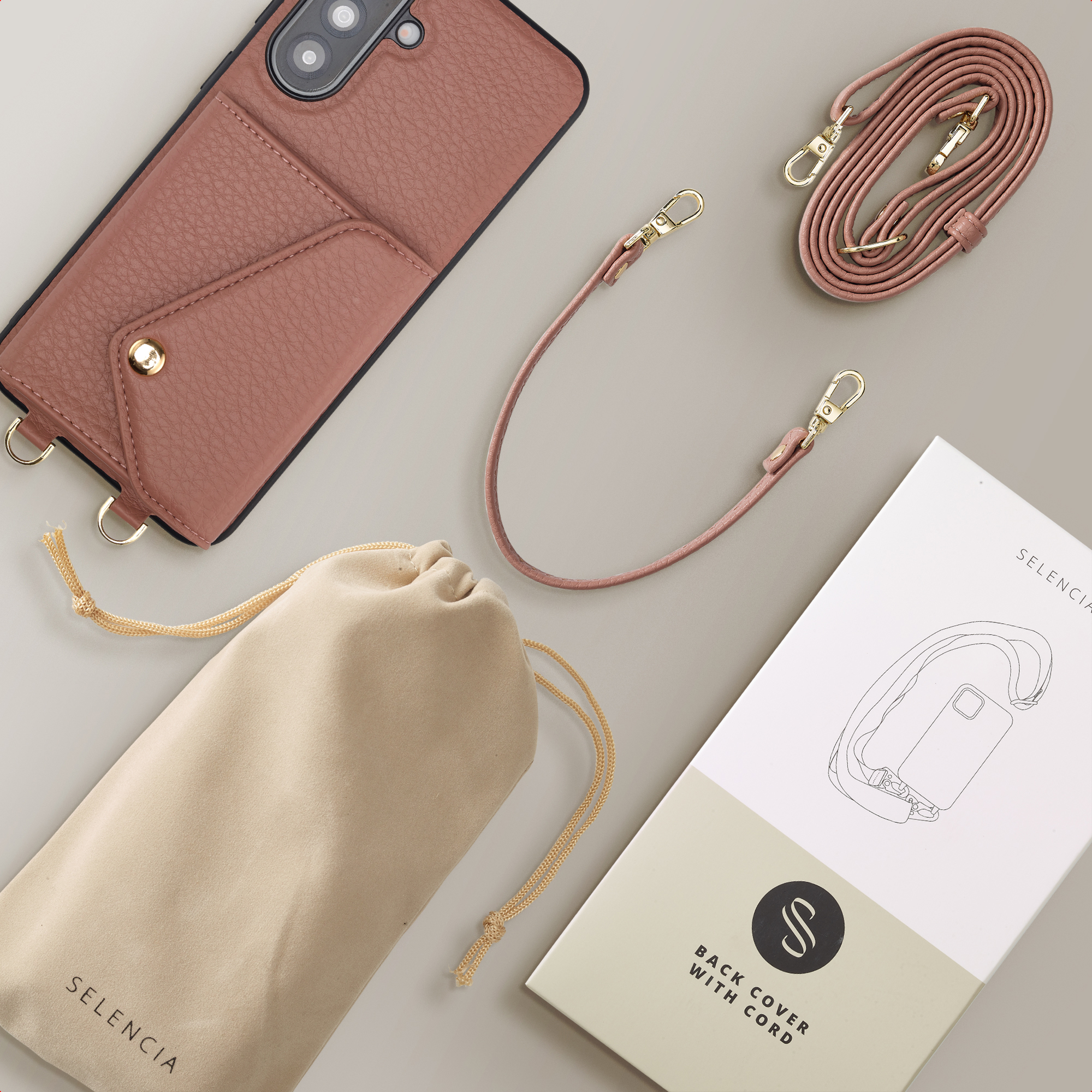Een roze telefoonhoes met zakje, een tasje en een band. Gouden accenten.
