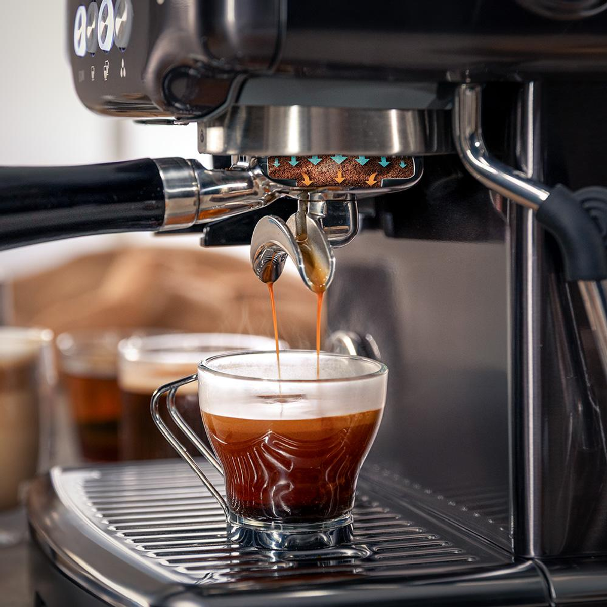 Una macchina per espresso eroga due flussi di caffè in una tazza di vetro.