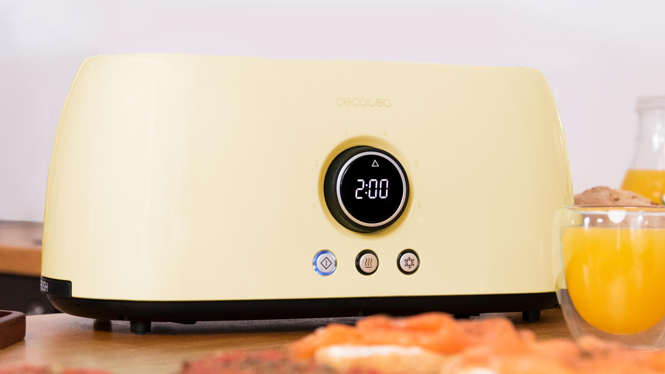Kremowy toster z cyfrowym wyświetlaczem (2:00) i szklankami soku pomarańczowego.