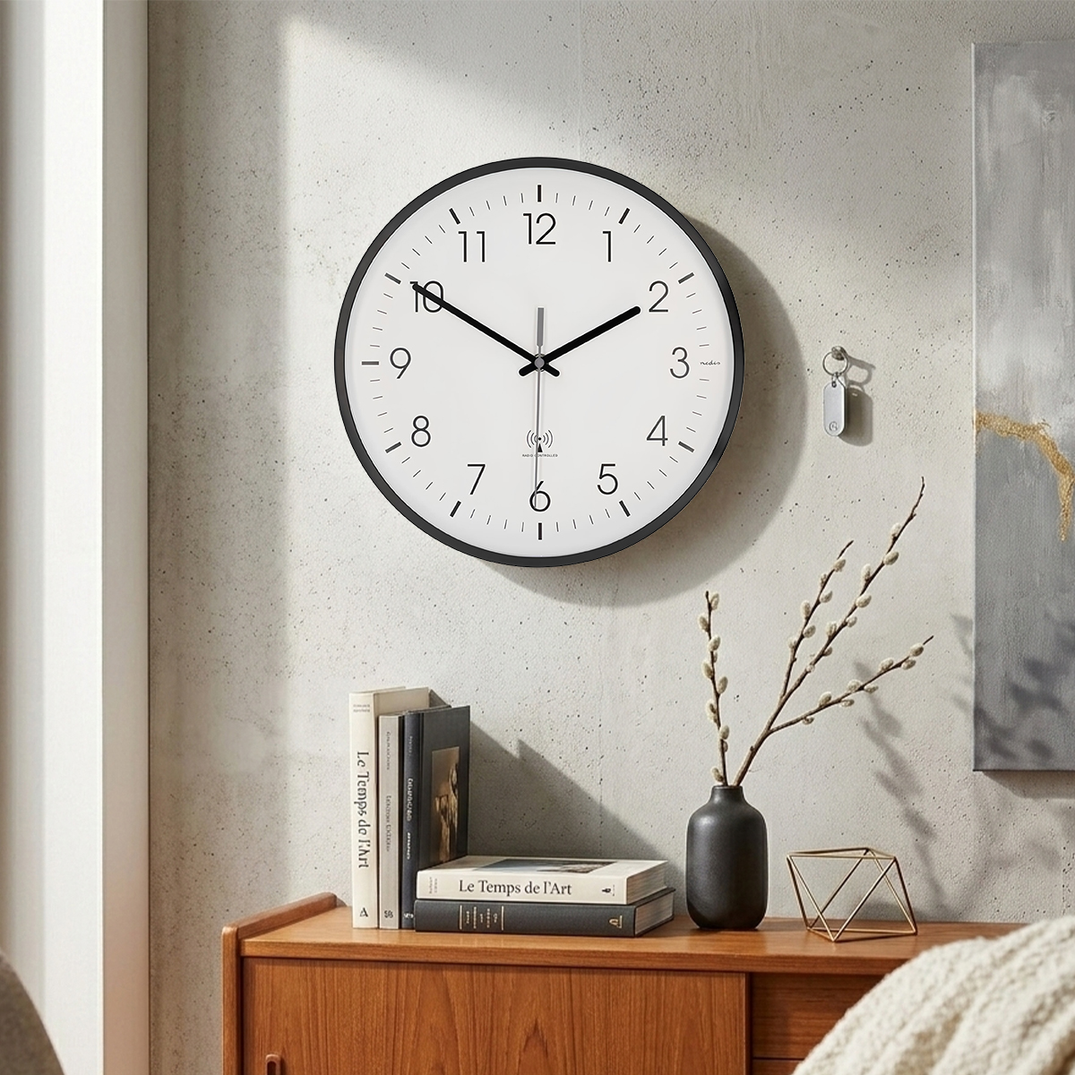 Eine Wanduhr mit schwarzem Rahmen und weißem Zifferblatt hängt über einem Holzschrank mit Büchern.