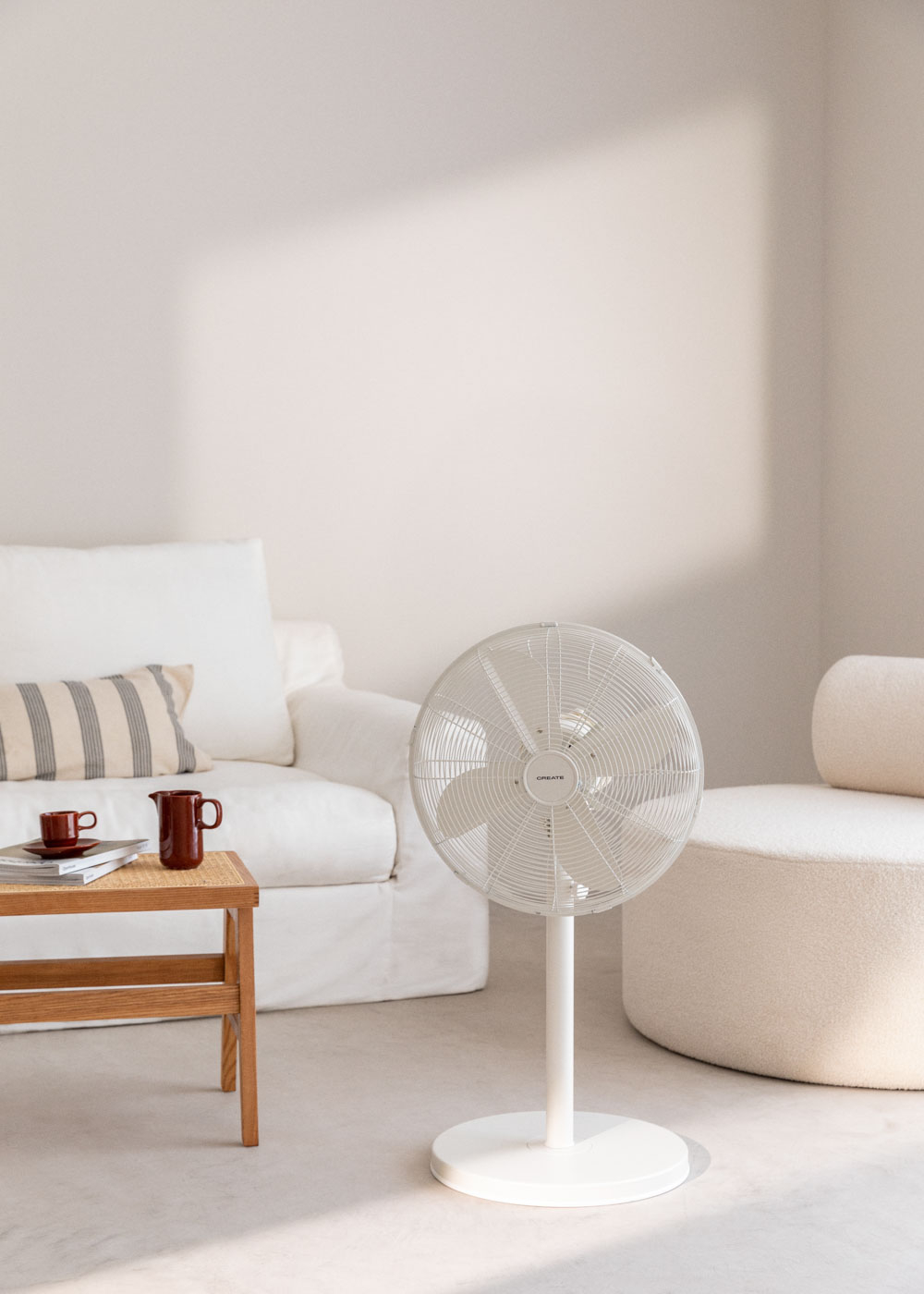Un ventilador de pie blanco está junto a un sofá blanco en una habitación minimalista.