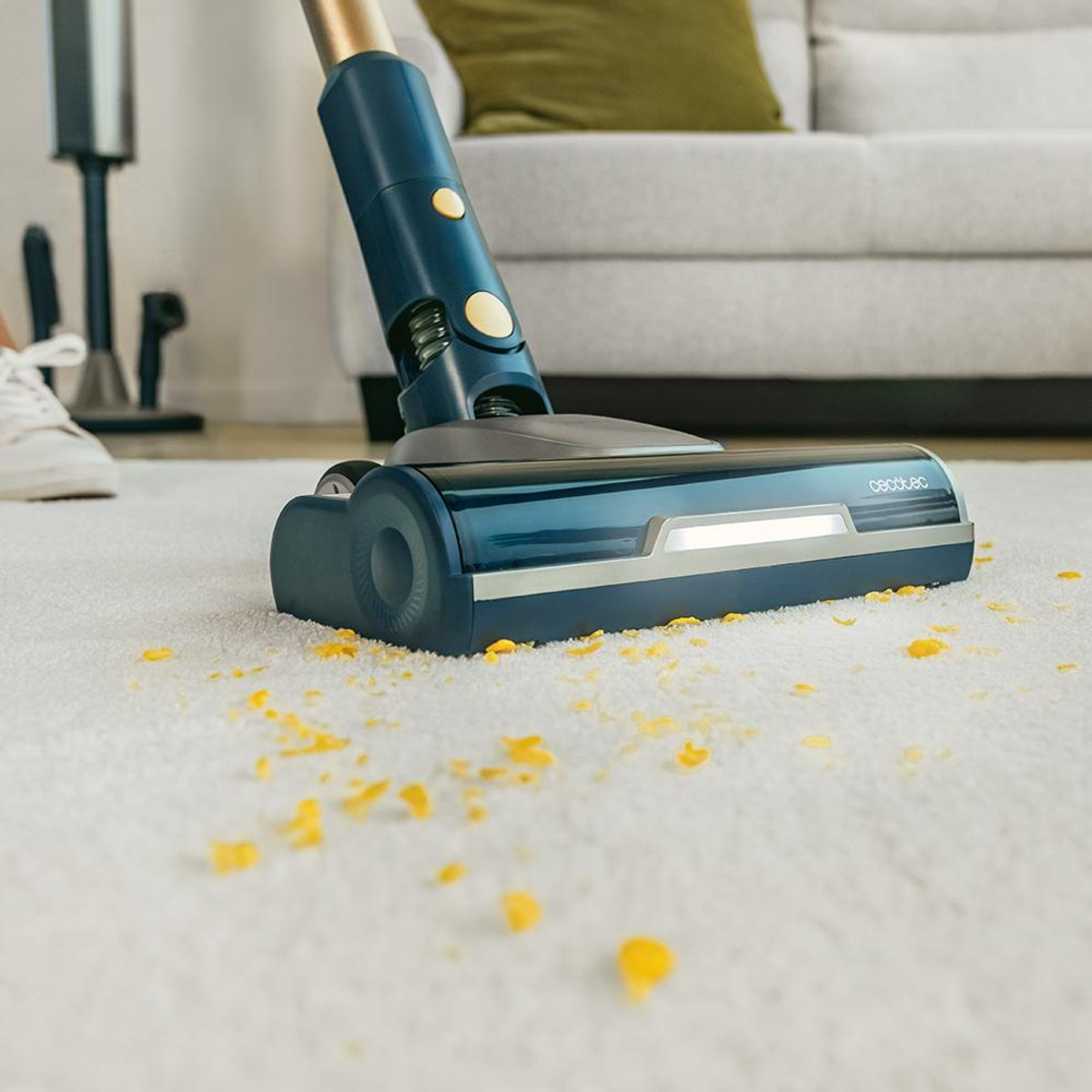 Un aspirapolvere blu pulisce un tappeto bianco con briciole gialle.