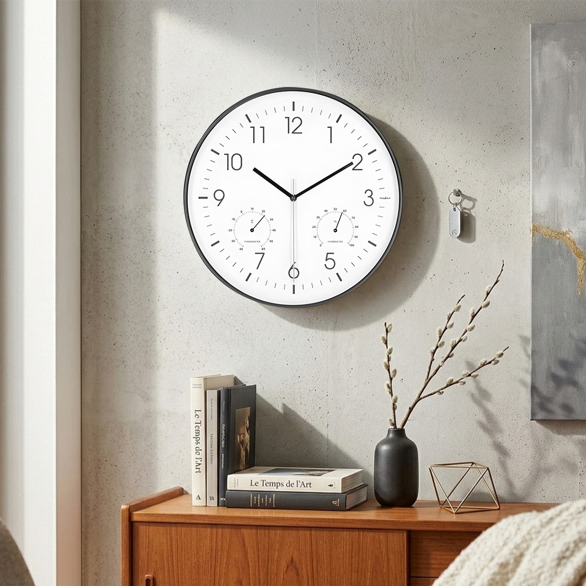 Eine weiße Wanduhr mit Thermometer und Hygrometer hängt an einer Betonwand.