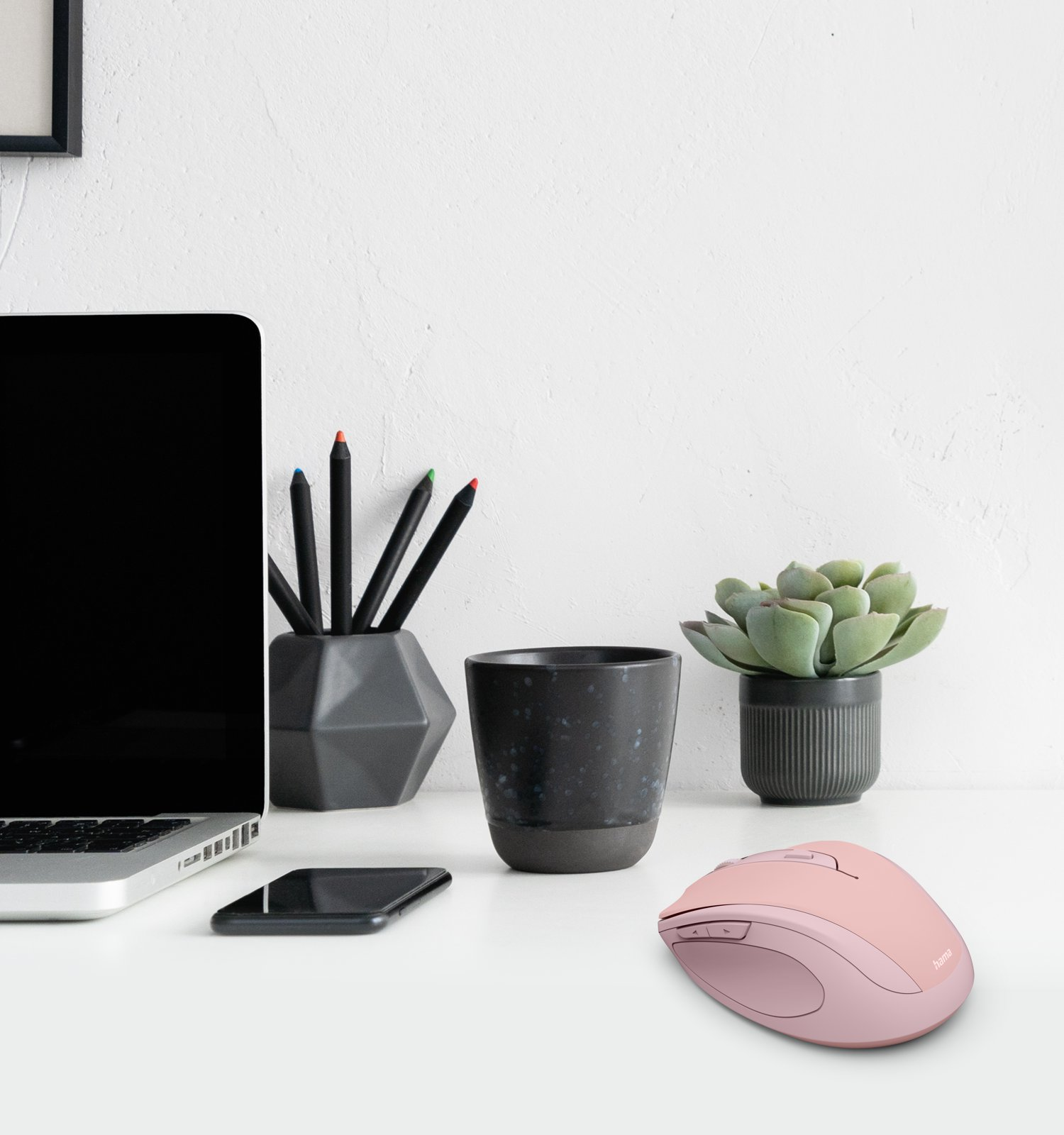 Un mouse rosa, laptop, telefono, penne e pianta su una scrivania.