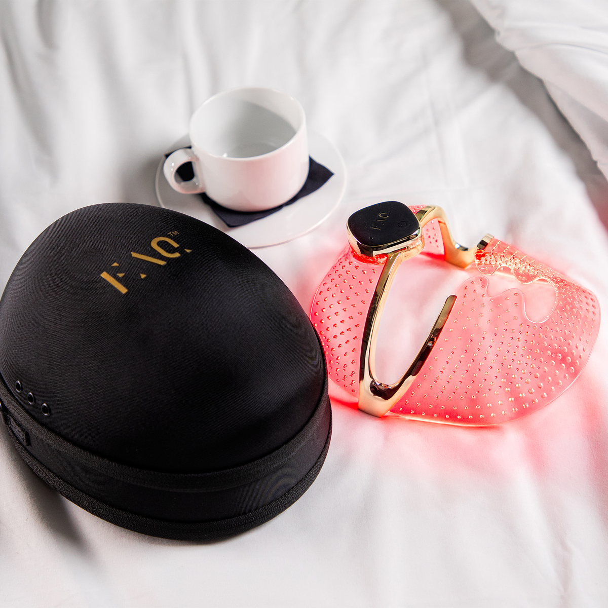 A black case, cup, and red device rest on a white sheet.