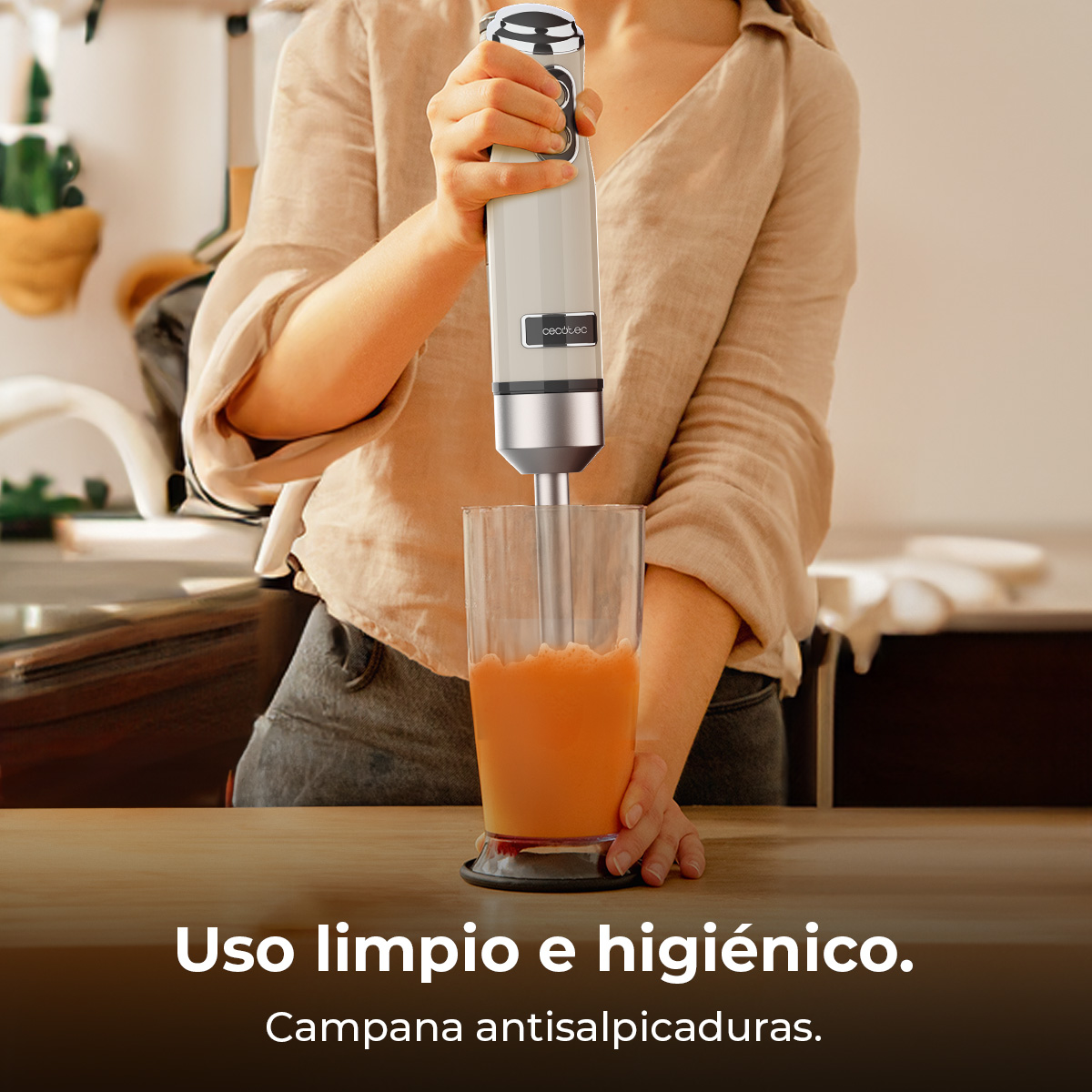 Una persona frulla una bevanda arancione in un bicchiere con un frullatore a immersione.