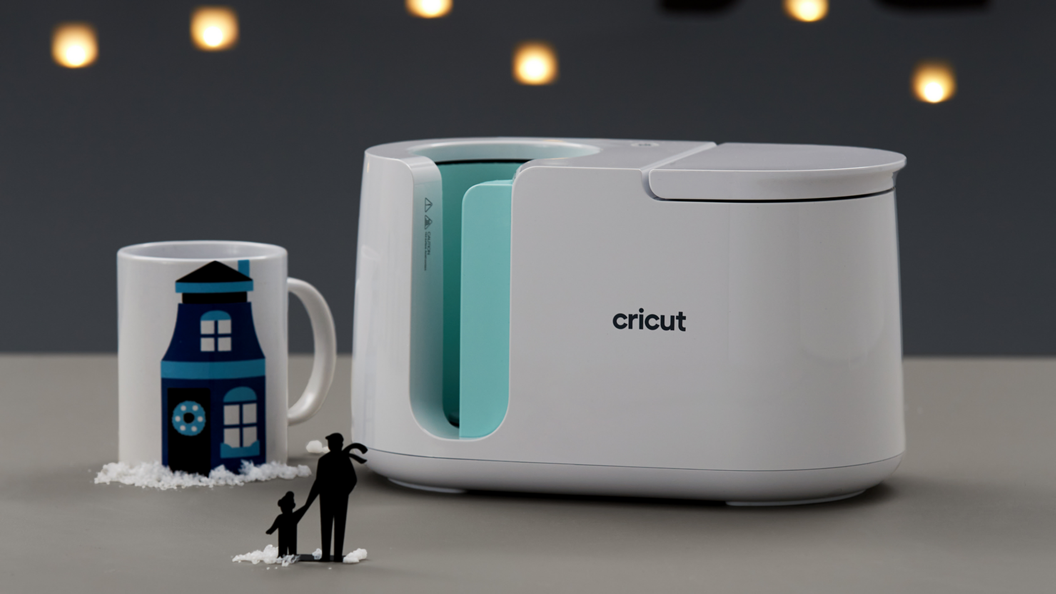 Una taza blanca con diseño de casa junto a una prensa Cricut blanca.