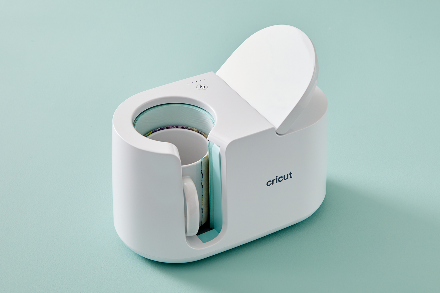 Una prensa de tazas Cricut blanca con una taza dentro, sobre fondo azul claro.