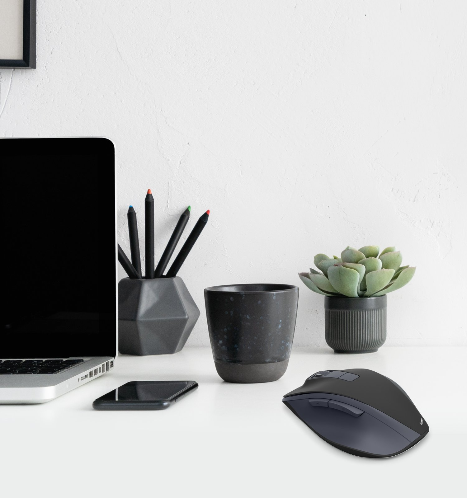 Una scrivania moderna con laptop, telefono, mouse, vaso e penne.