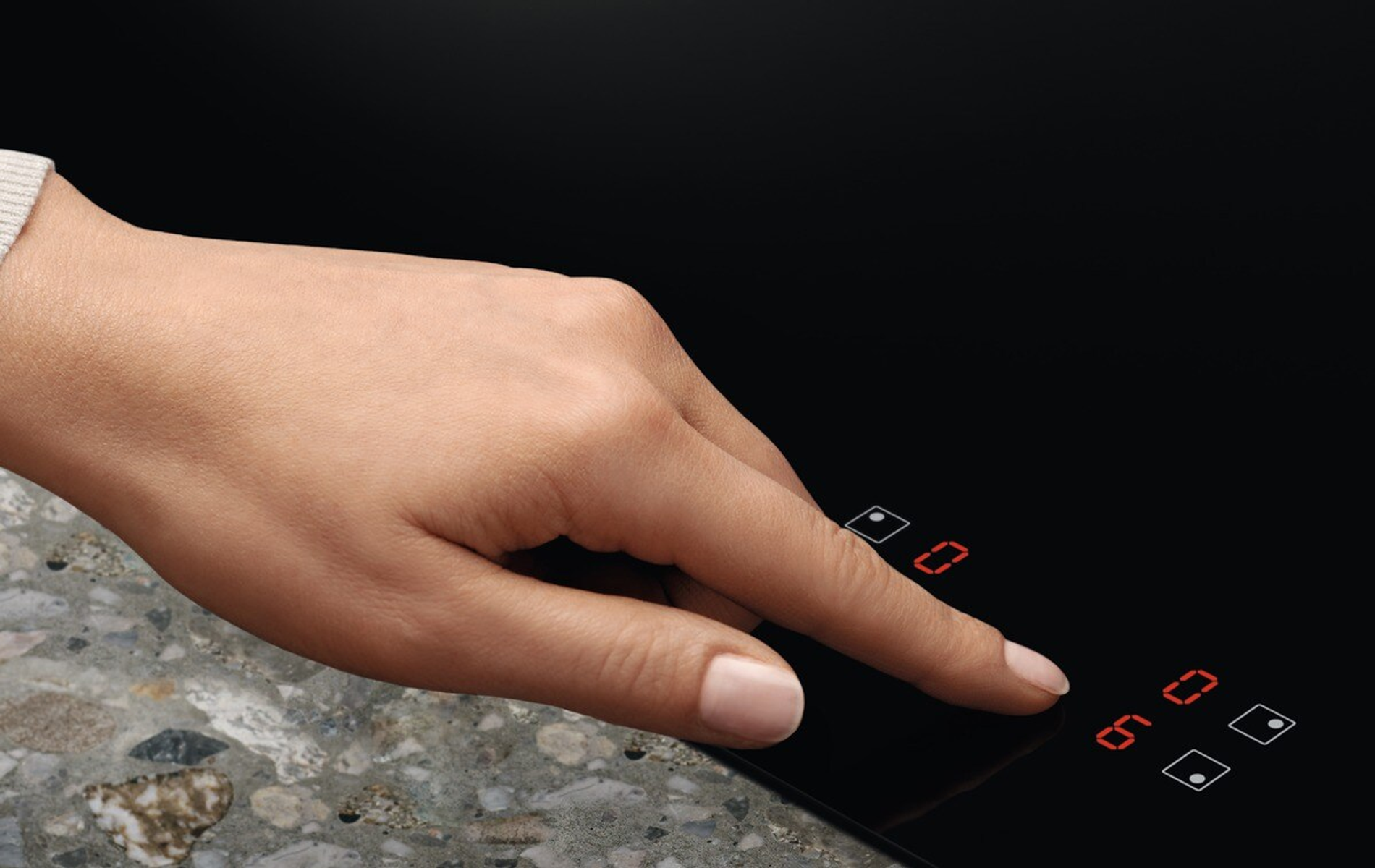 Una mano tocca un piano cottura con display digitali rossi.