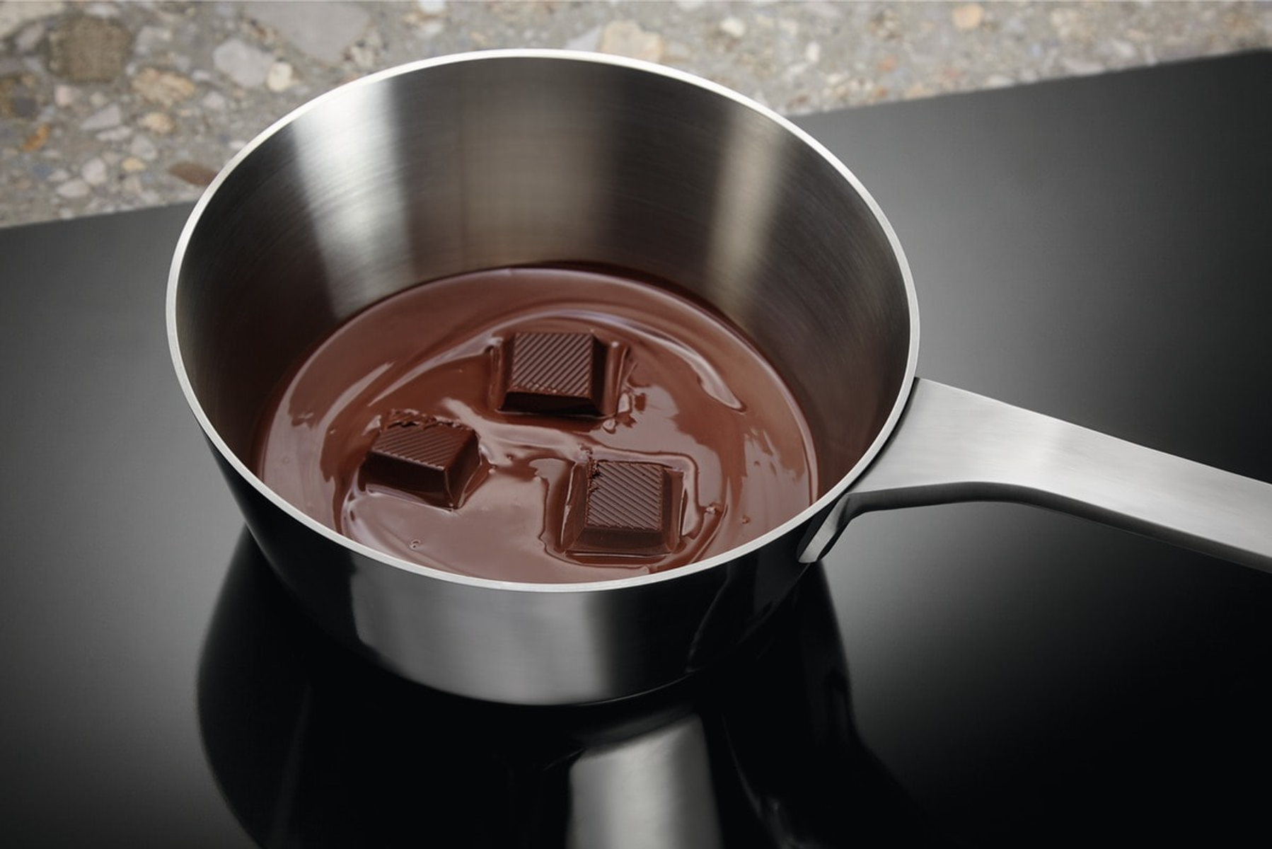 Cioccolato che si scioglie in una pentola di metallo su un fornello nero.