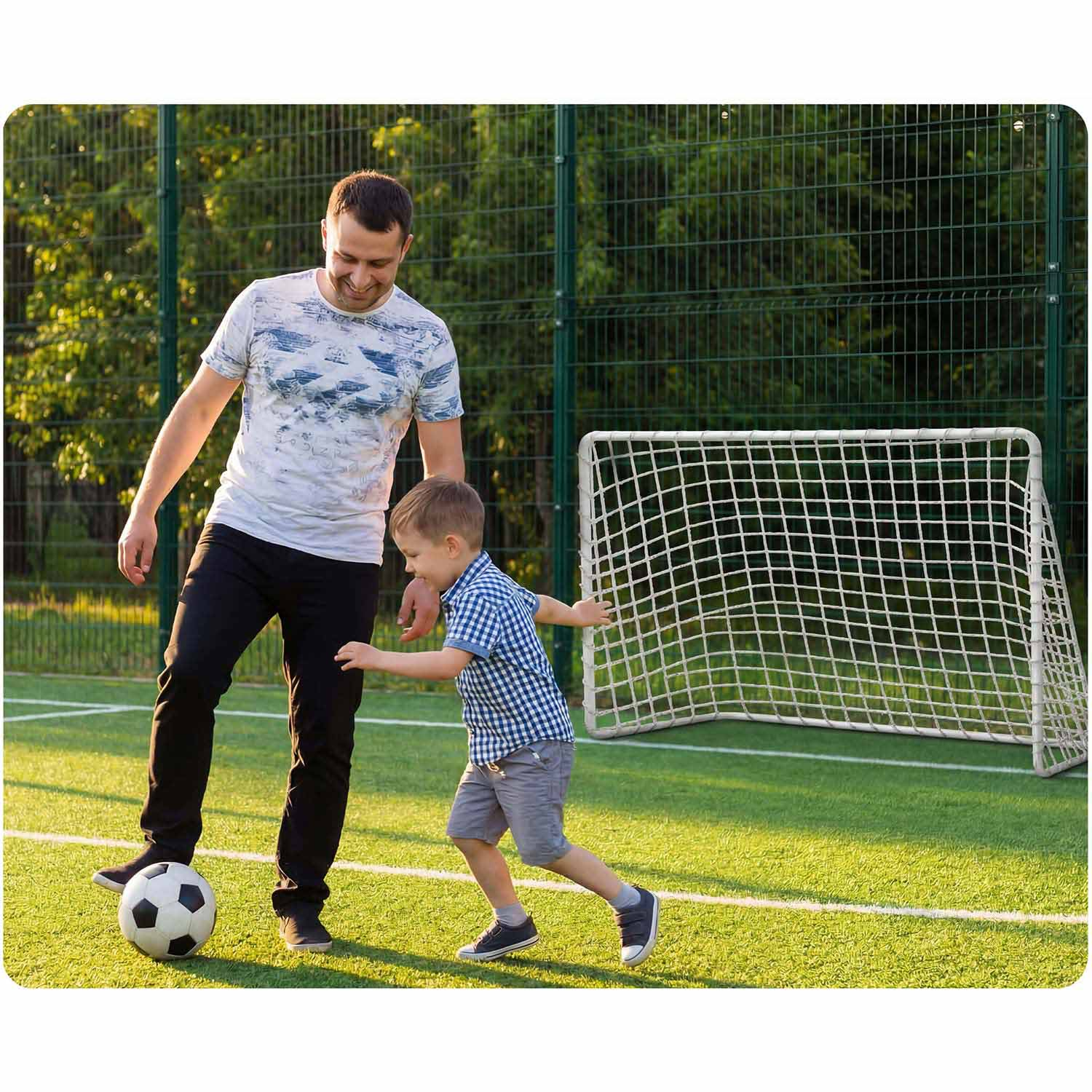 Mężczyzna i chłopiec grają w piłkę nożną na sztucznej trawie z bramką.