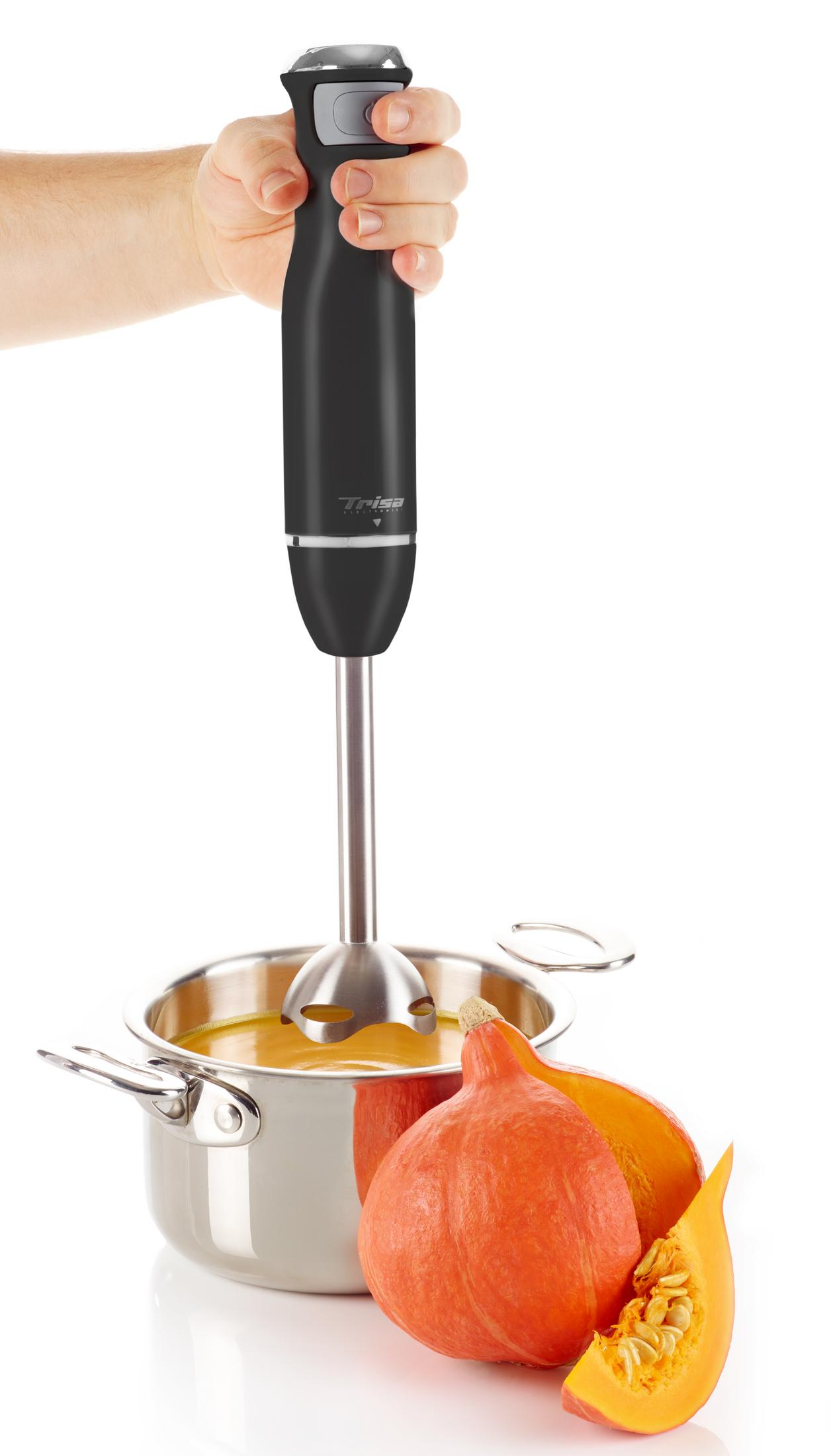 Hand hält schwarzen Stabmixer über Topf mit Suppe; daneben Kürbisse.