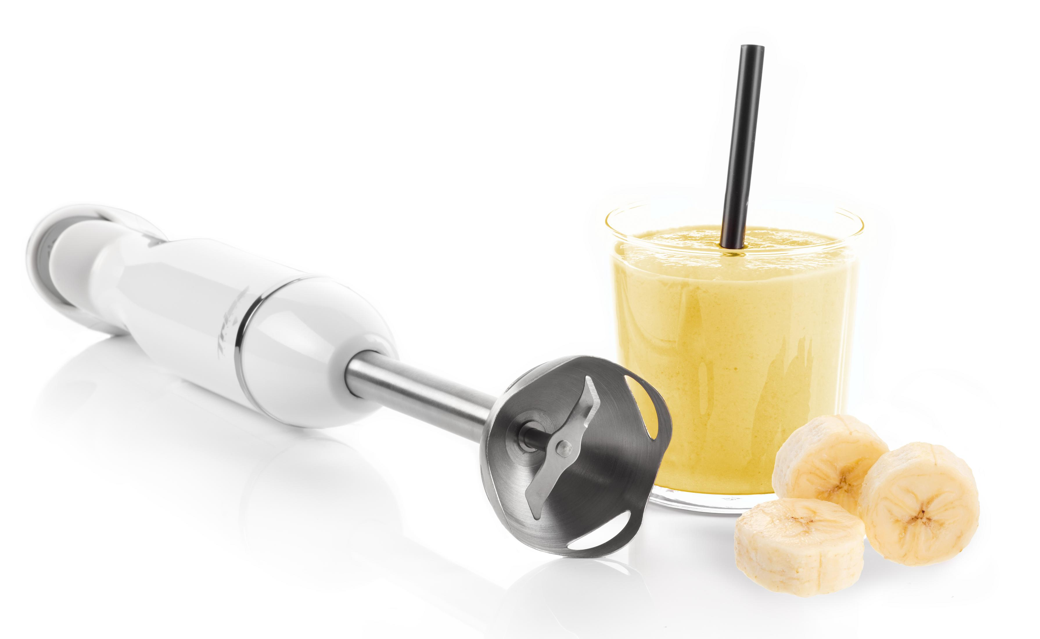 Ein weißer Stabmixer liegt neben einem Glas Bananensmoothie mit Strohhalm und Bananenstücken.