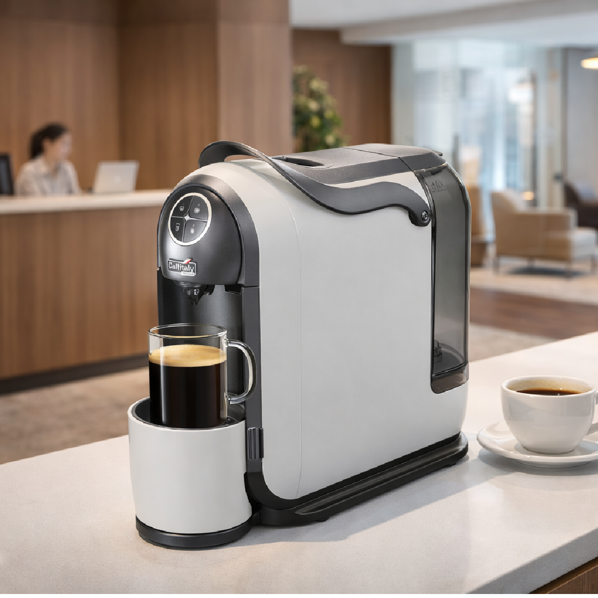 Eine weiß-graue Kaffeemaschine brüht Kaffee in einen Glasbecher. Eine zweite Tasse steht daneben.