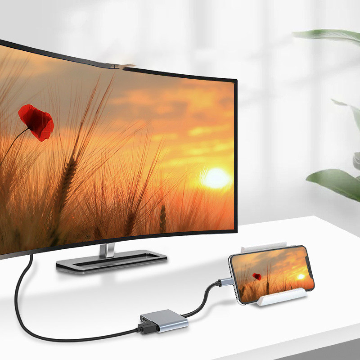 Zakrzywiony monitor i smartfon wyświetlają zachód słońca nad polami pszenicy z czerwonym makiem.