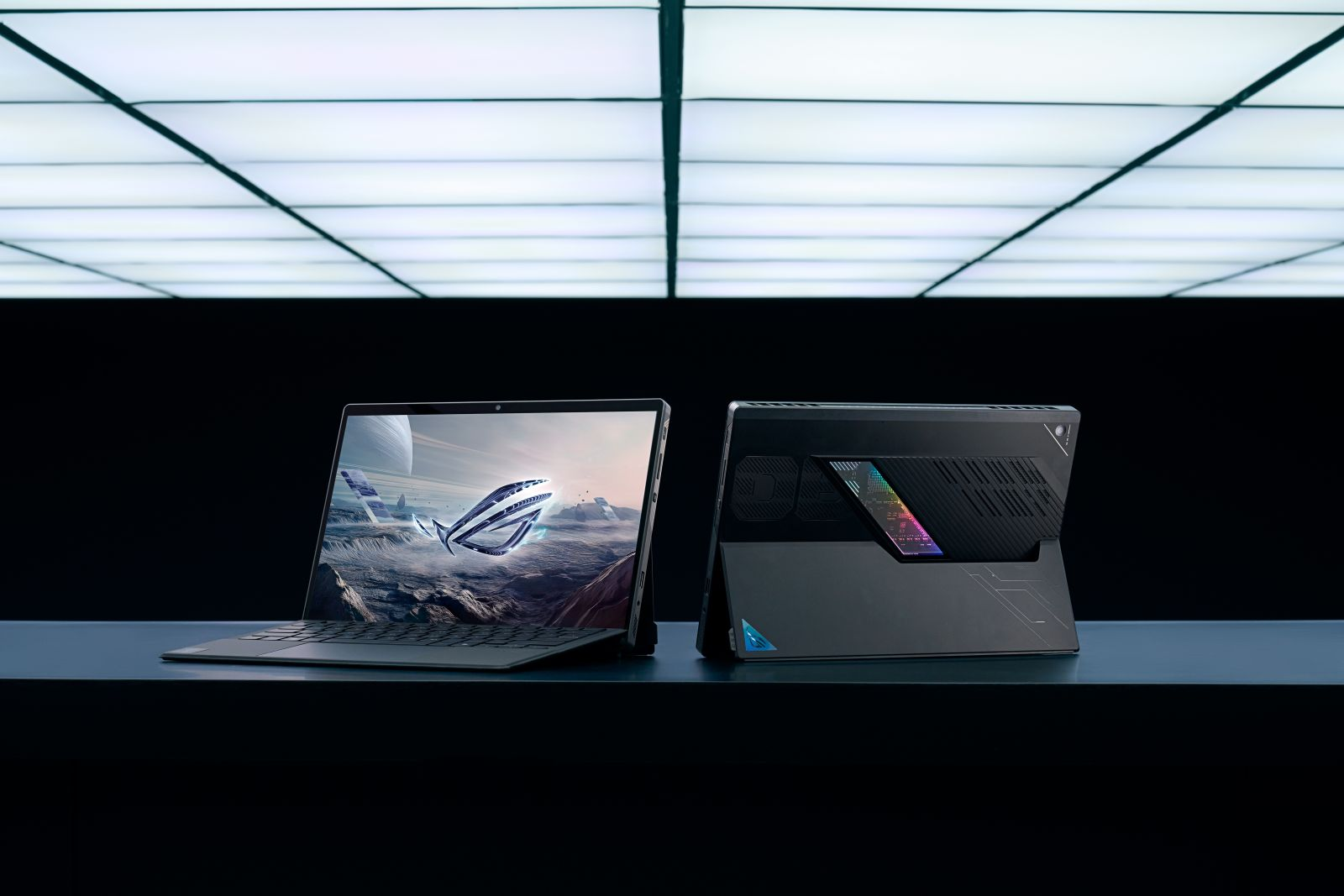 Dwa laptopy obok siebie. Jeden otwarty z grą na ekranie, drugi zamknięty z podświetlonym logo.
