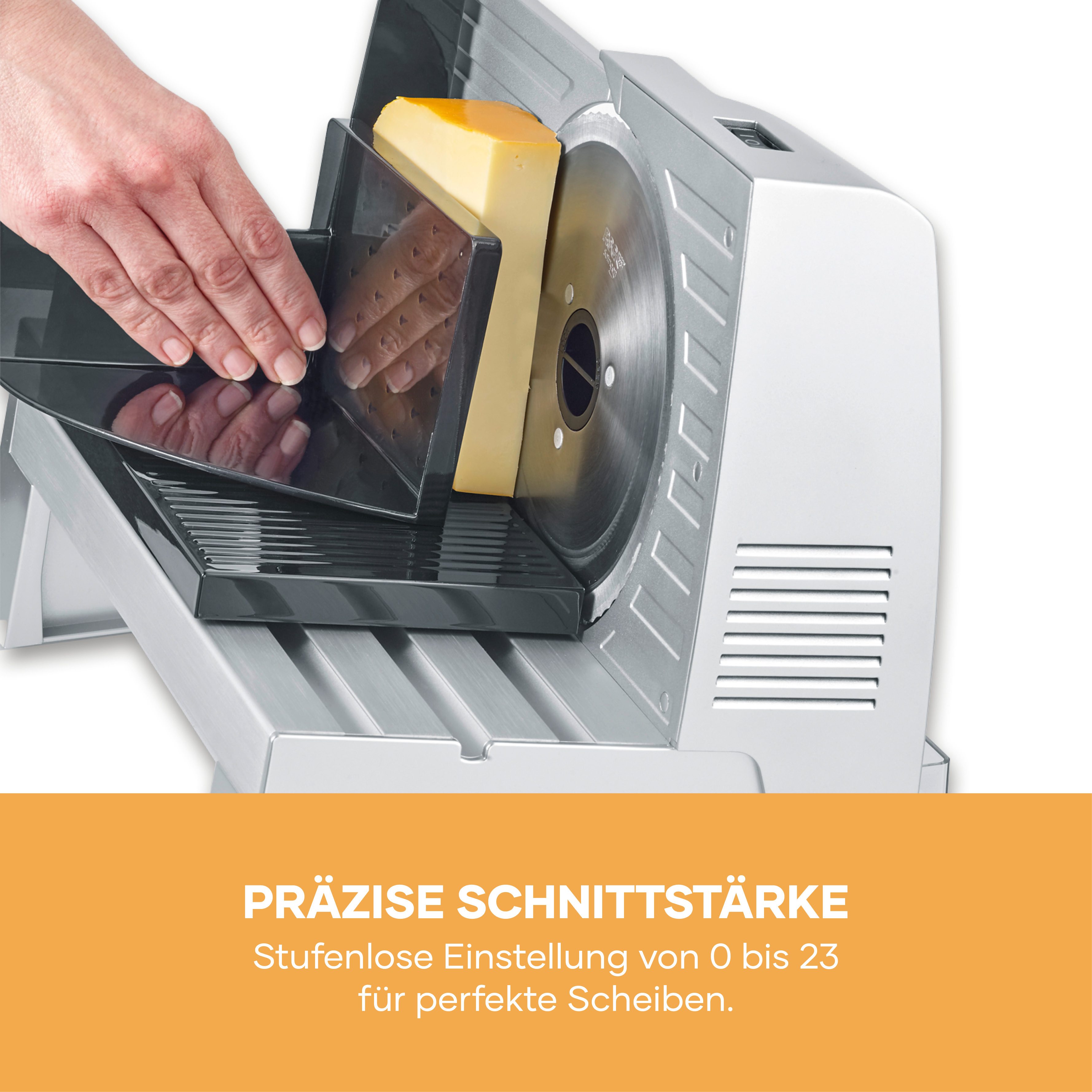 Eine Hand schiebt einen Käseblock auf einen elektrischen Schneider mit Klinge.