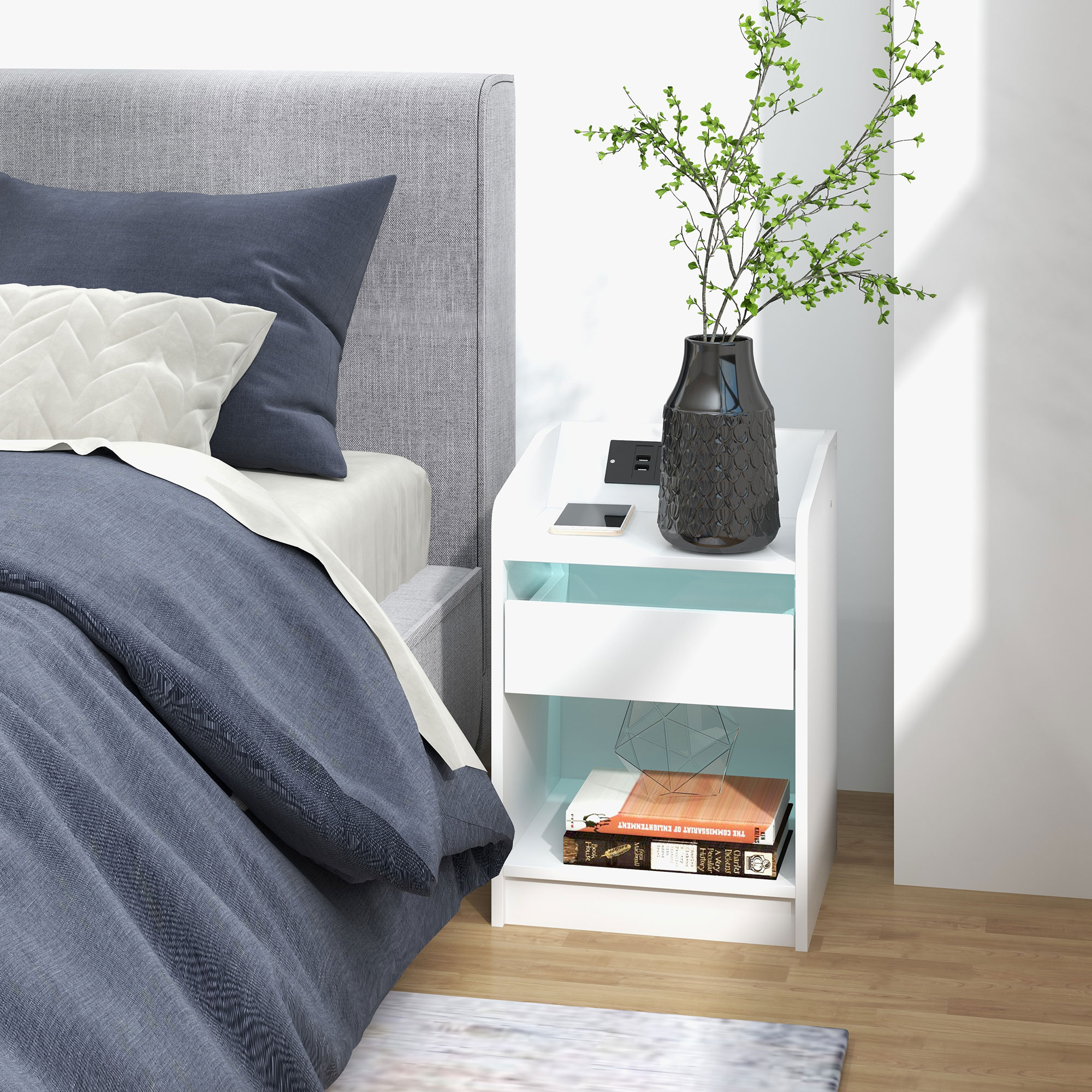 Una mesita de noche blanca con cajón junto a una cama con ropa de cama azul y blanca.