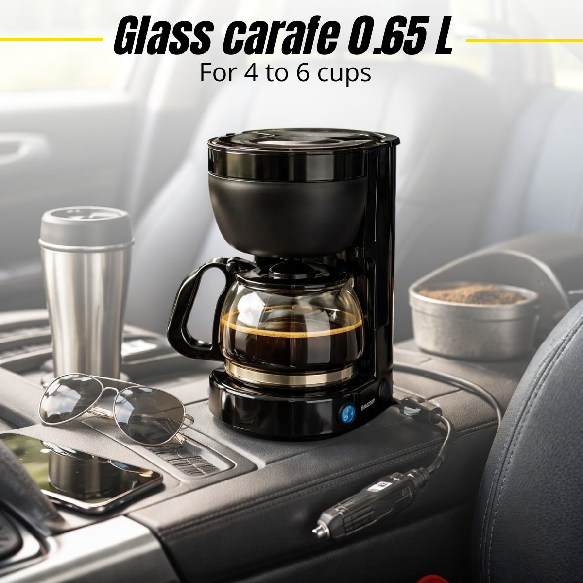 Car coffee maker with glass carafe, coffee, mug, sunglasses, and phone on console.