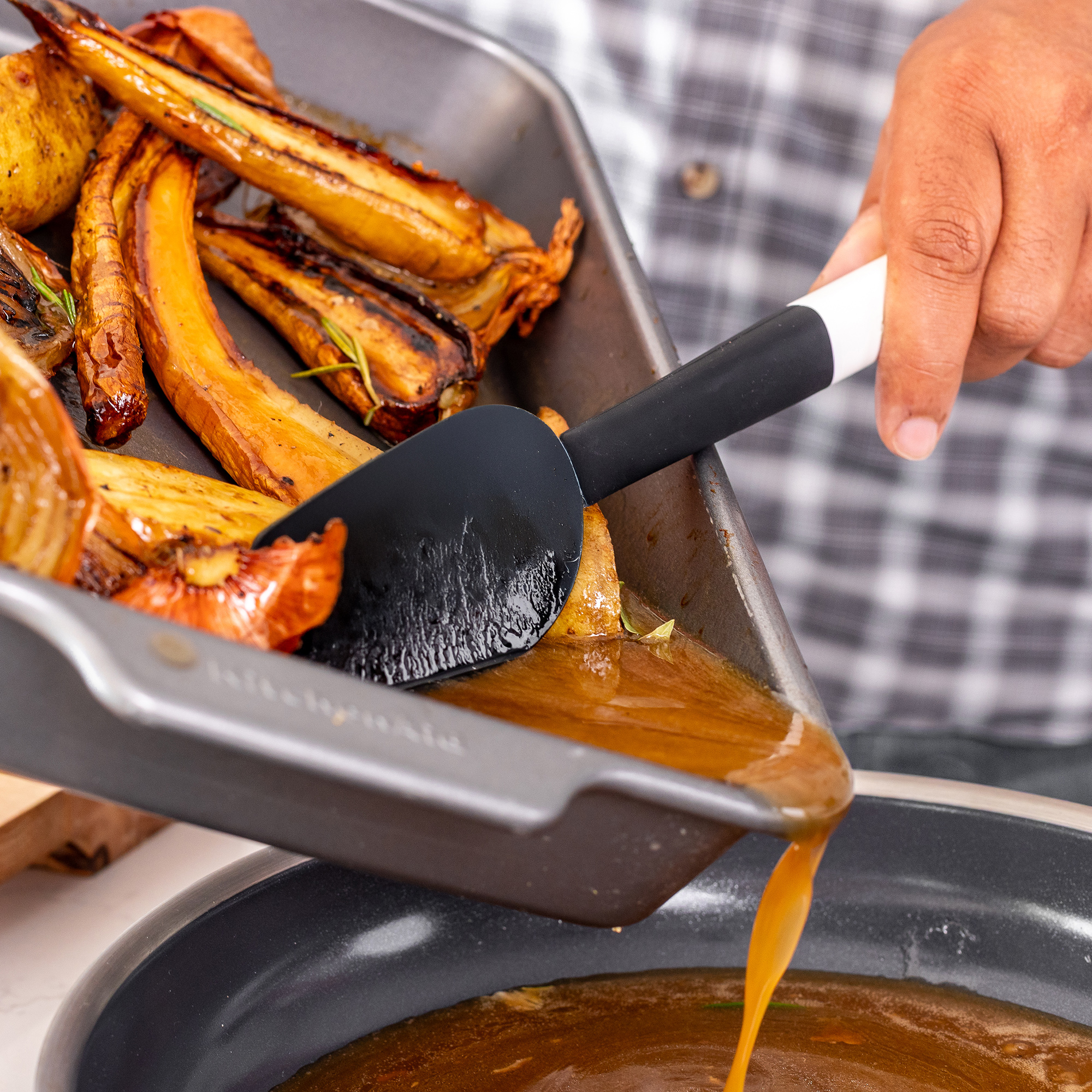 Geröstetes Wurzelgemüse wird mit Saft aus einer Auflaufform in eine Pfanne gegossen.