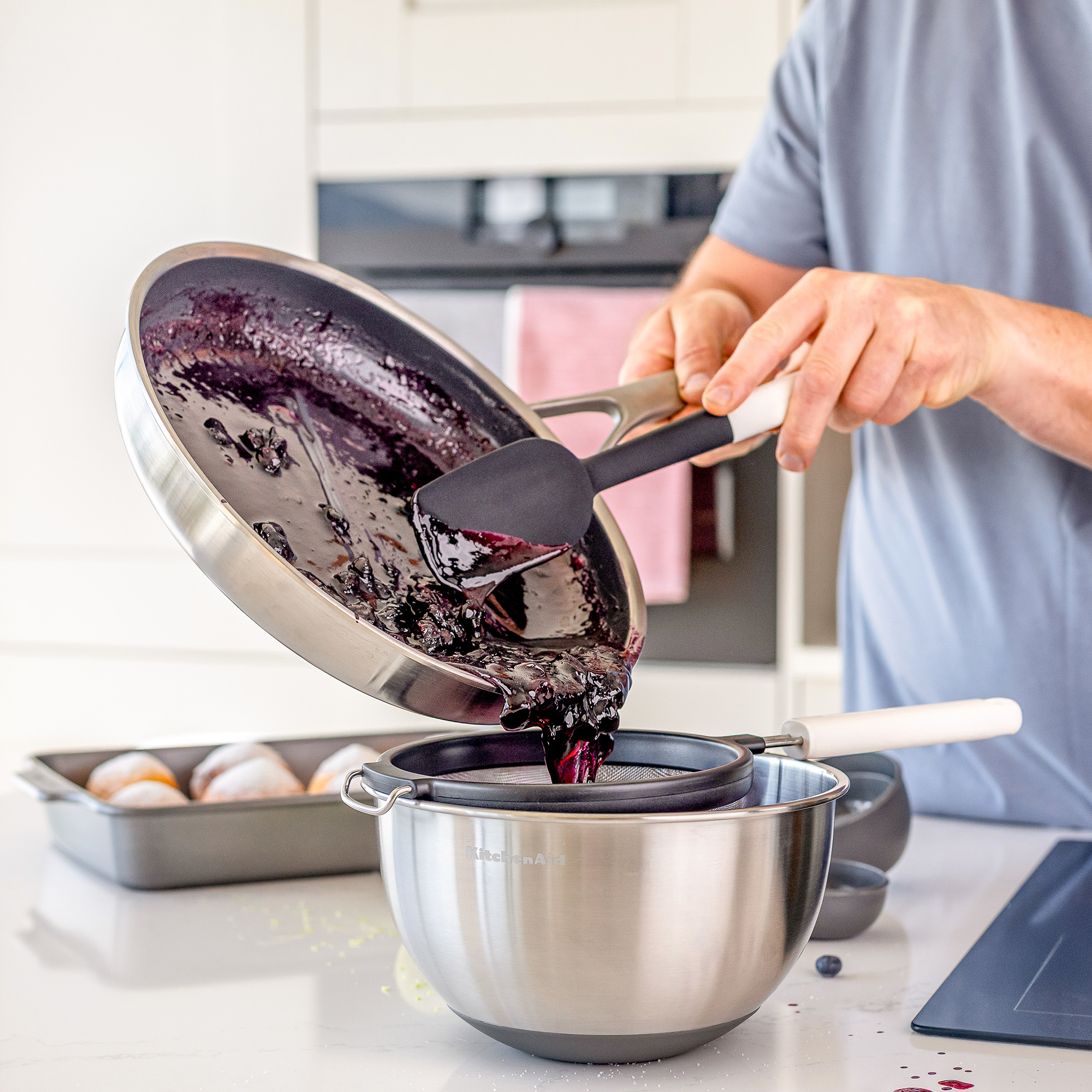 Blaubeersauce wird aus einer Pfanne in ein Sieb über einer Schüssel gegossen.
