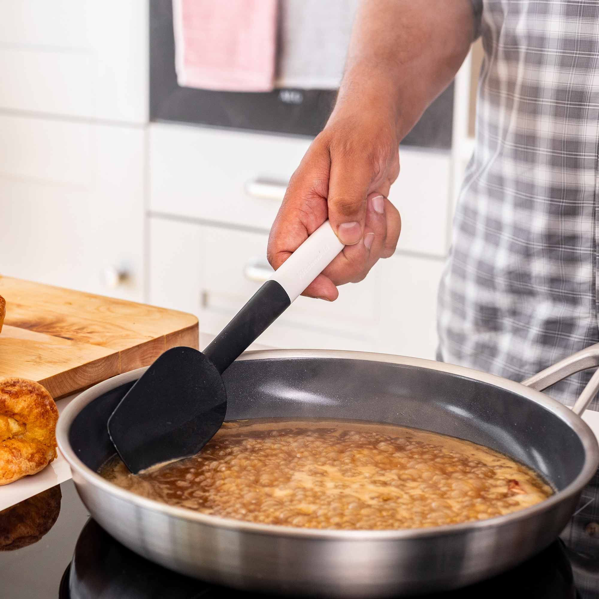 Eine Person rührt mit einem schwarzen Spatel in einer Pfanne mit kochender Sauce.