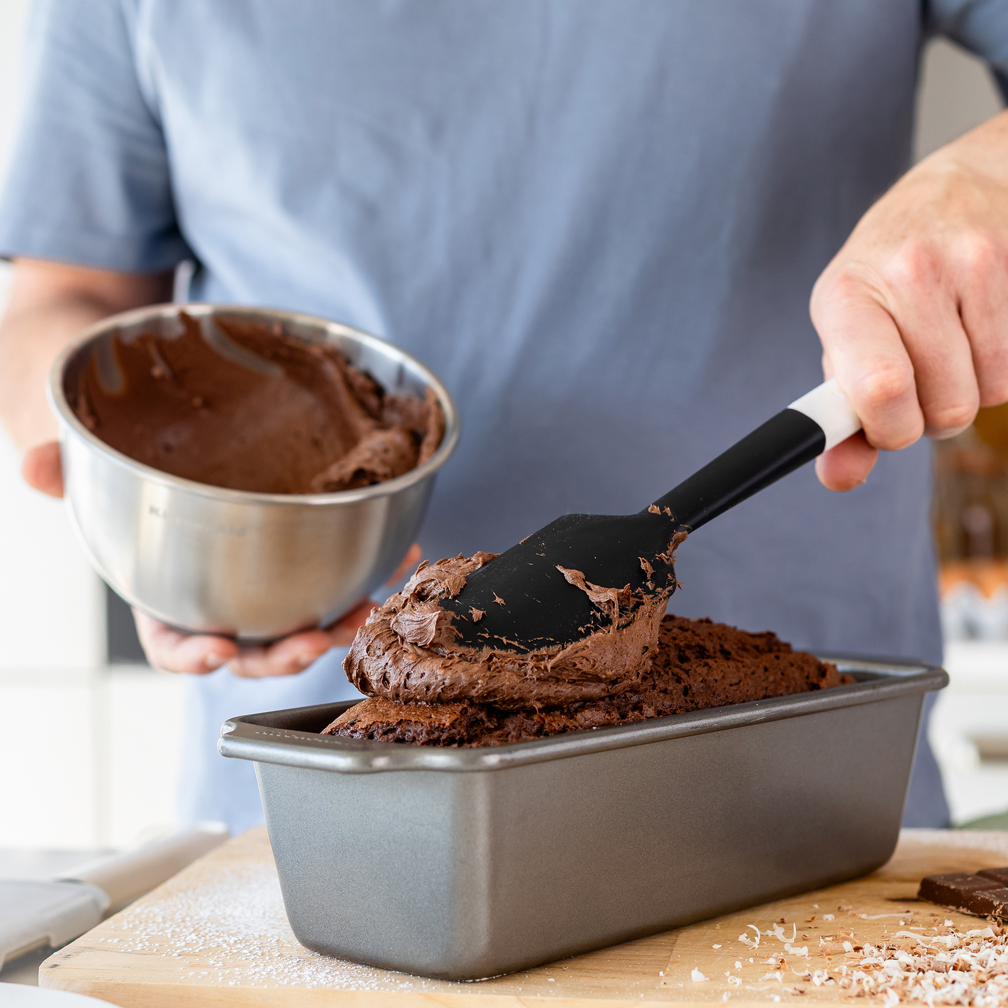 Schokoladenkuchenteig wird mit einem Spatel in eine Kastenform gegeben.