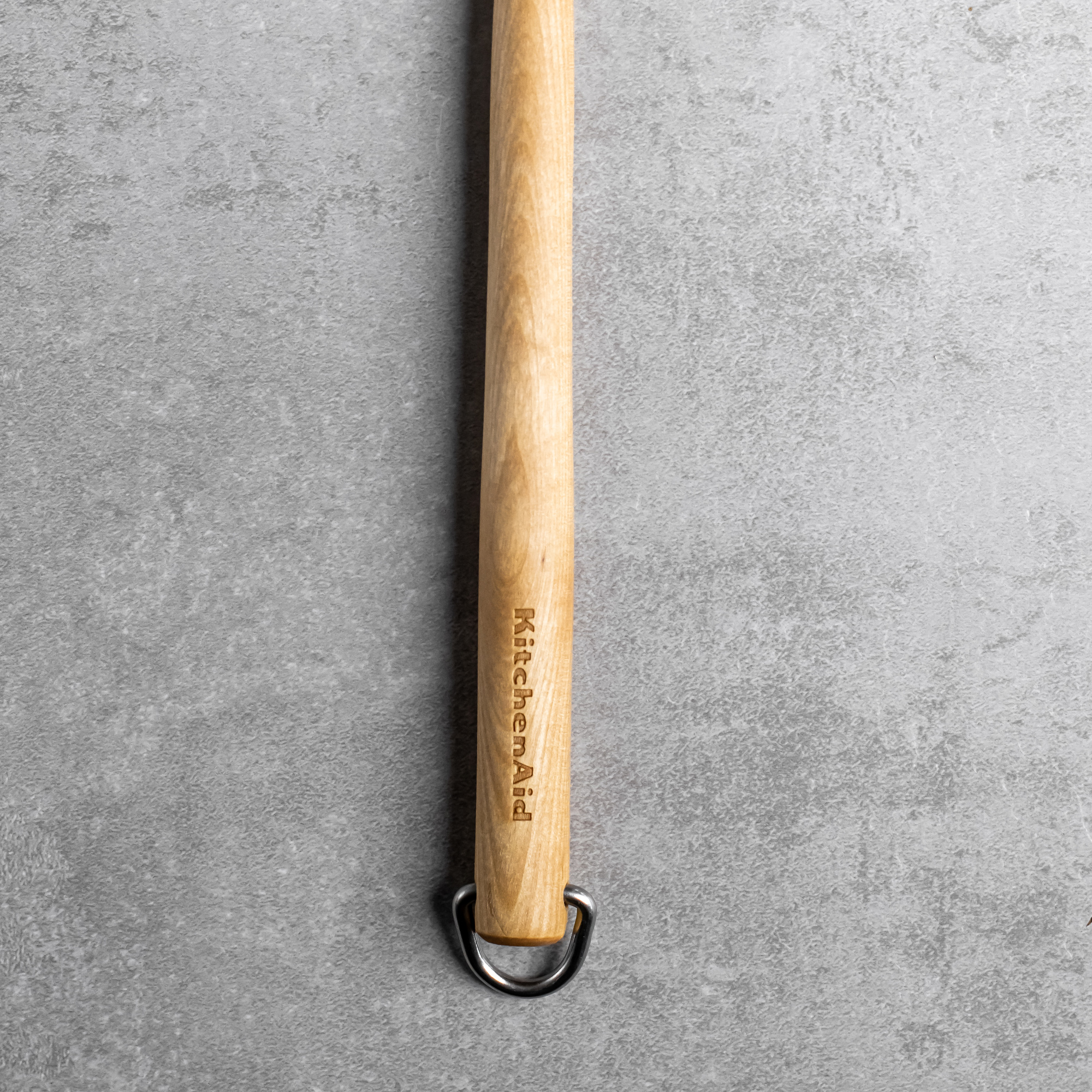 Holzgriff mit KitchenAid-Logo und Metallring auf grauem Untergrund.