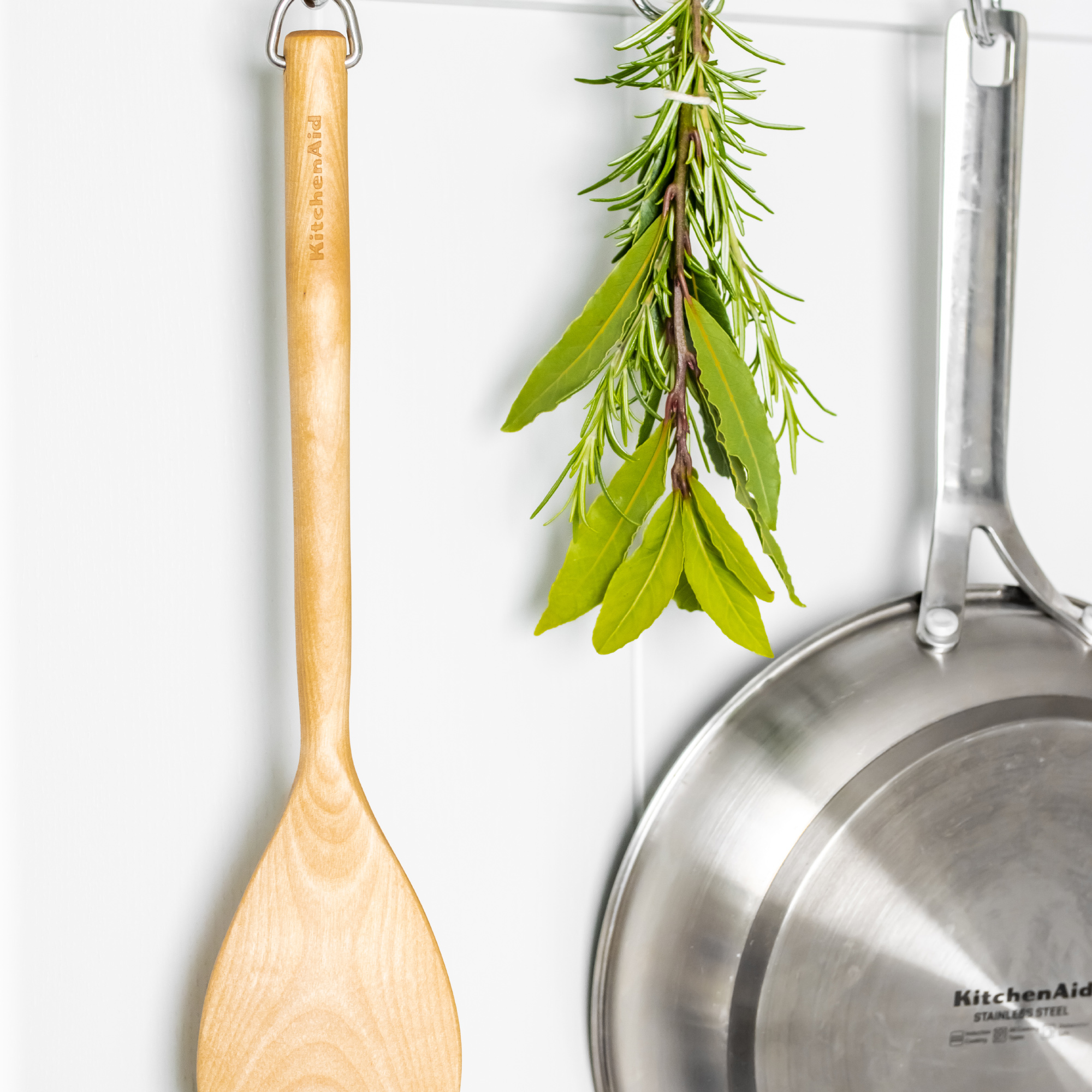 Holzlöffel, Kräuter und Pfanne hängen an einer Wand.