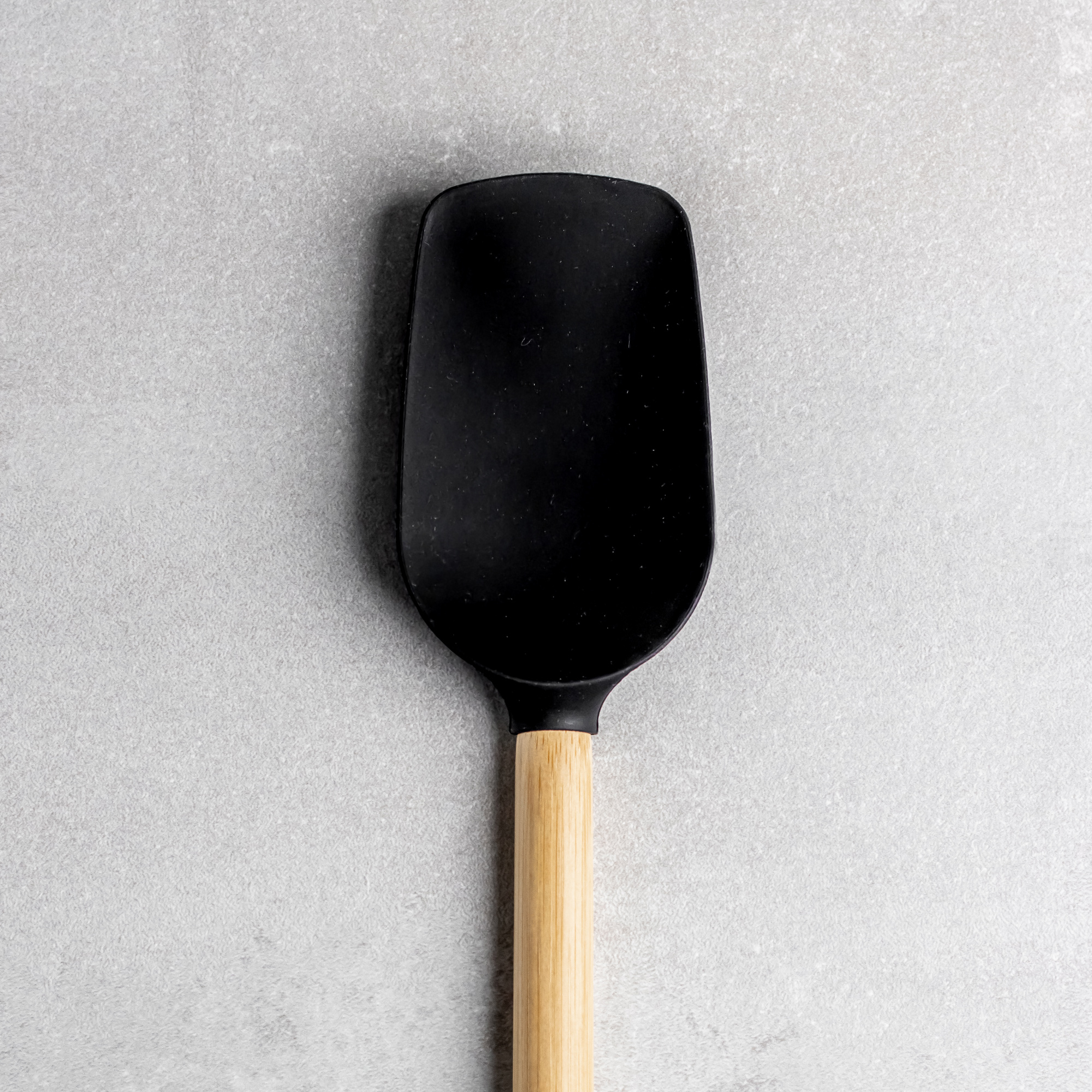 Ein schwarzer Silikonspatel mit Holzgriff auf grauem Hintergrund.