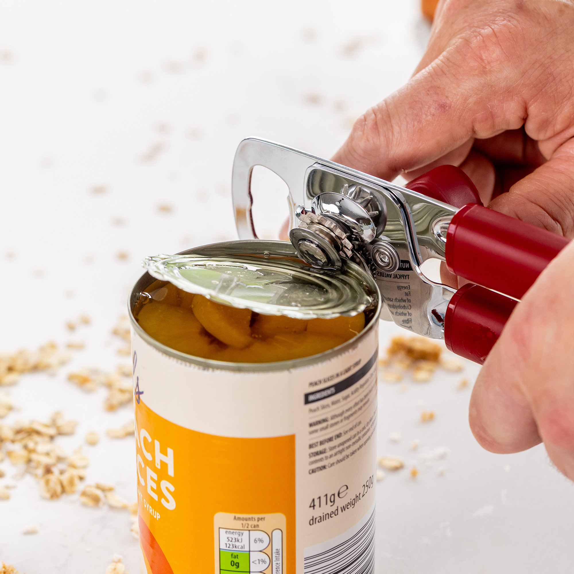 Eine Person öffnet eine Dose Pfirsichstücke in Sirup mit einem roten Dosenöffner.